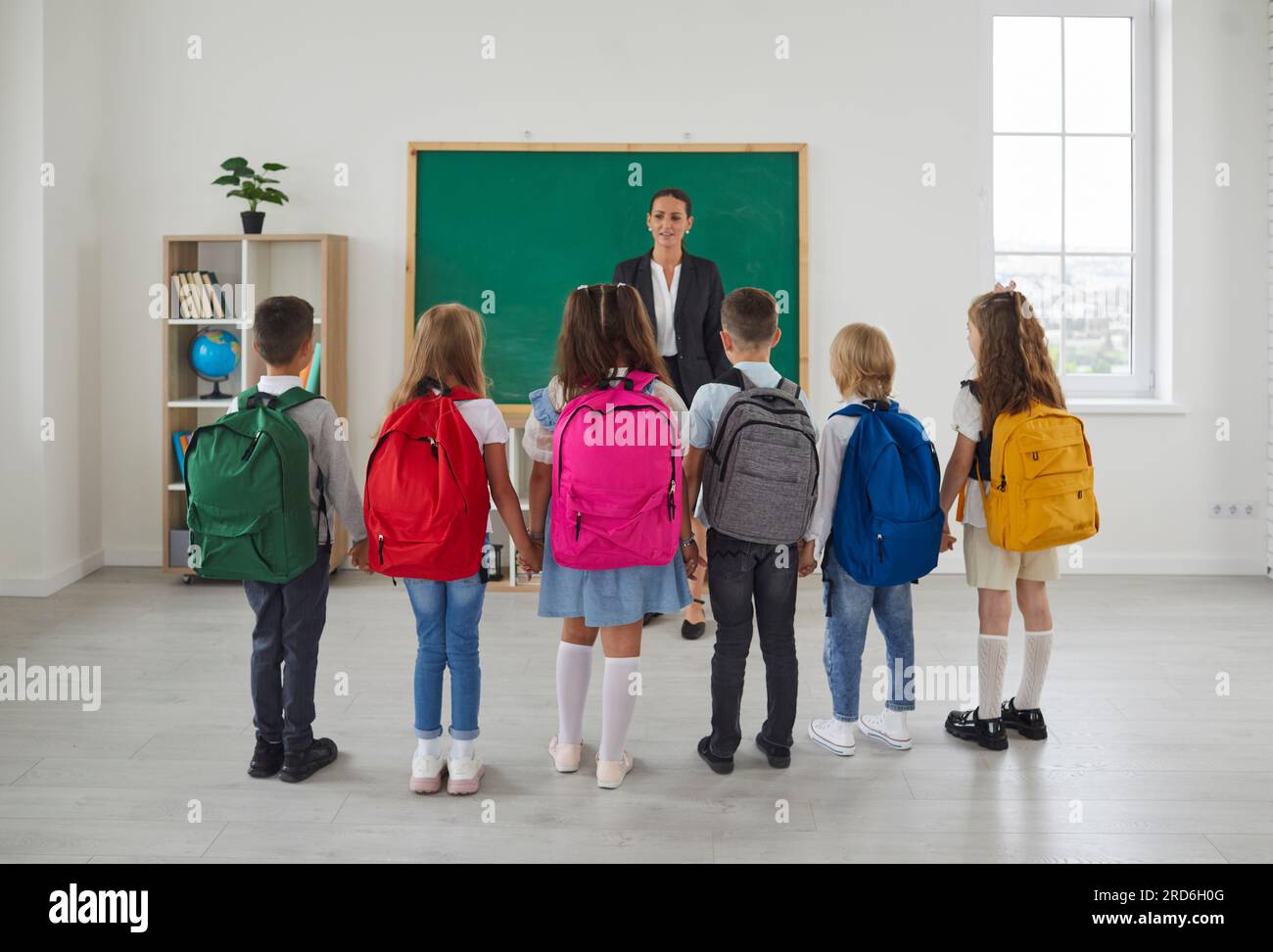 Gruppo di compagni di classe in piedi intorno all'insegnante in classe prima della lezione o il primo giorno di scuola. Foto Stock