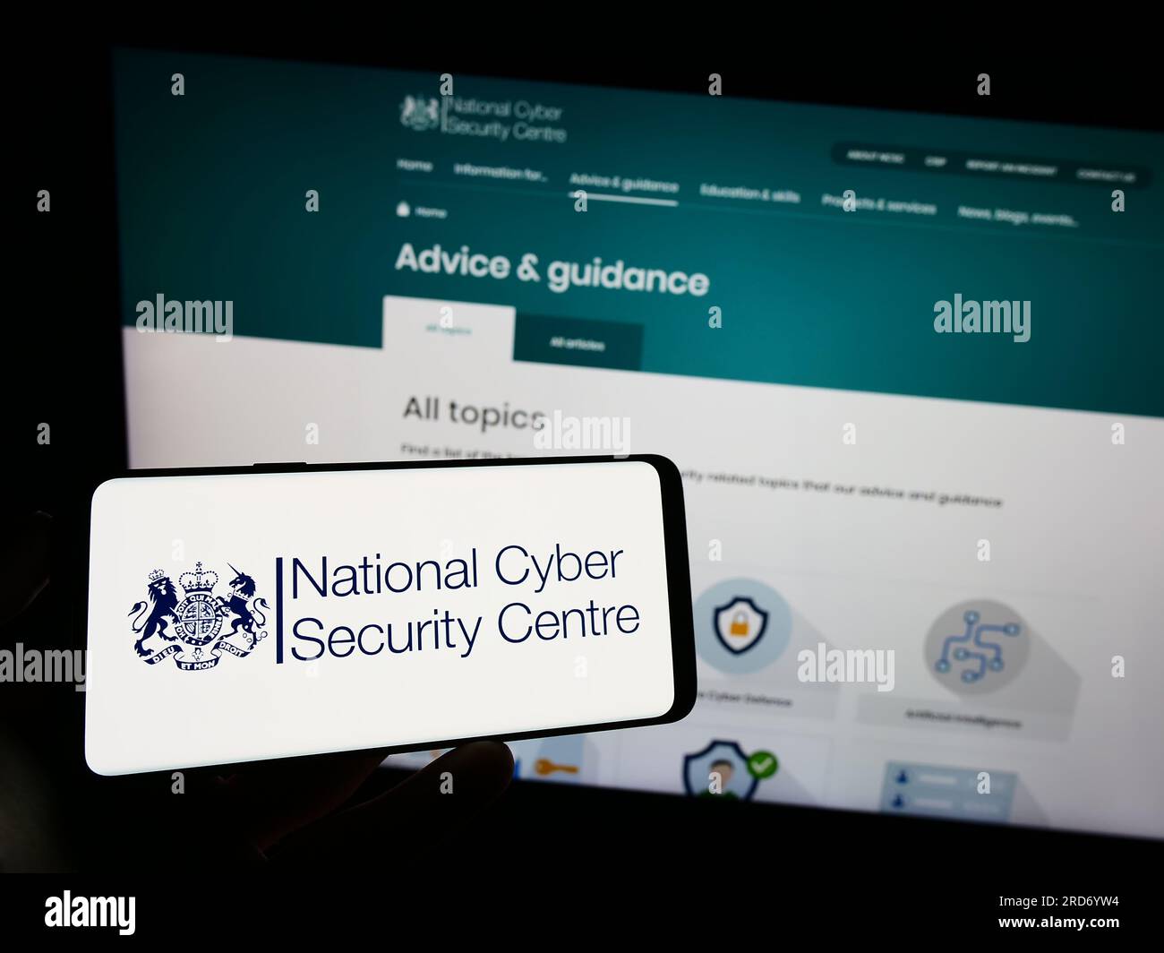 Persona in possesso di un cellulare con il logo del British National Cyber Security Centre (NCSC) sullo schermo davanti alla pagina Web. Concentrarsi sul display del telefono. Foto Stock