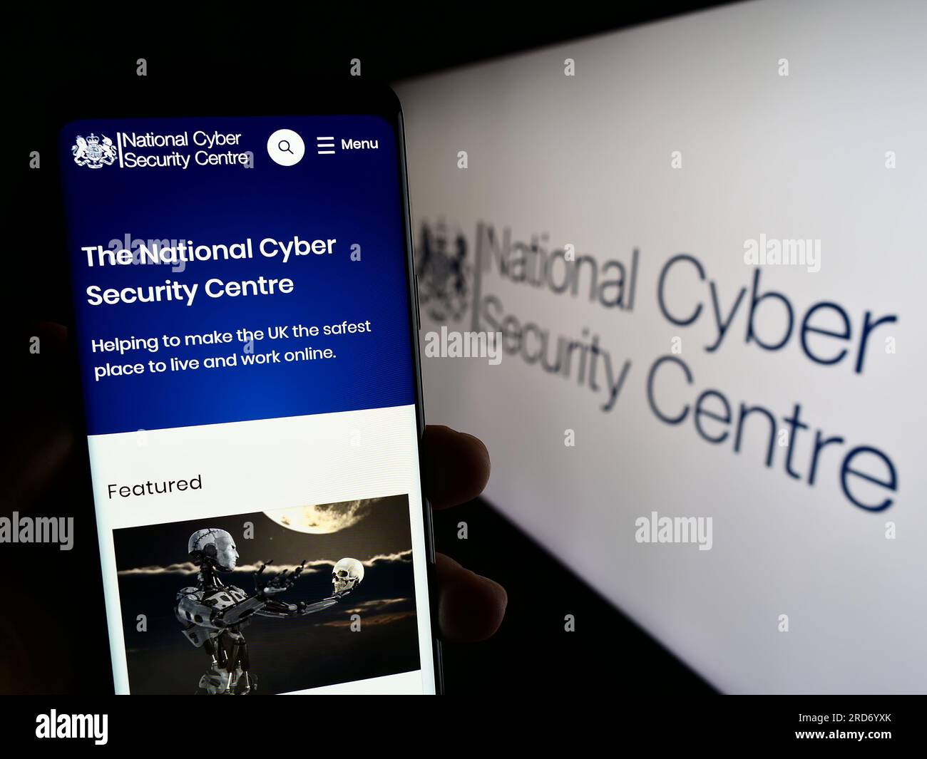 Persona che possiede uno smartphone con una pagina Web del National Cyber Security Centre (NCSC) del Regno Unito sullo schermo davanti al logo. Concentrarsi sul centro del display del telefono. Foto Stock
