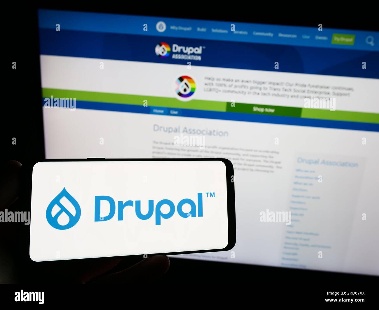 Persona che possiede uno smartphone con il logo del sistema di gestione dei contenuti Drupal sullo schermo di fronte al sito Web. Concentrarsi sul display del telefono. Foto Stock