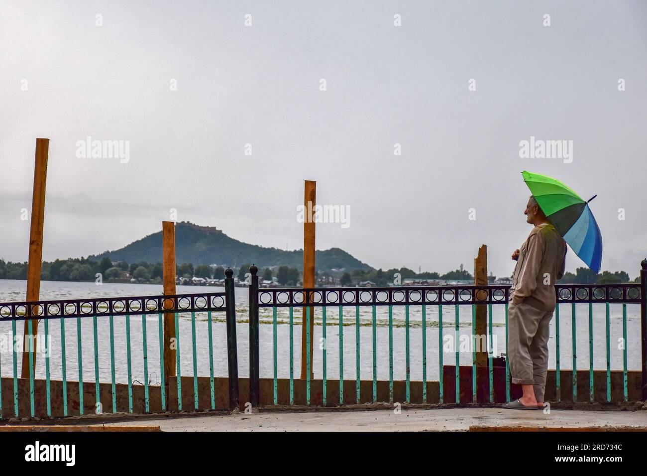 Un uomo tiene un ombrello mentre si trova sulle rive del lago dal durante le piogge a Srinagar, la capitale estiva di Jammu e Kashmir. Credito: SOPA Images Limited/Alamy Live News Foto Stock