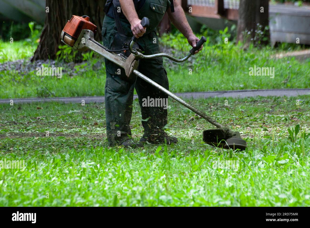 Lavoratore che taglia l'erba con un tagliaerba a benzina nel parco  cittadino o nel cortile.