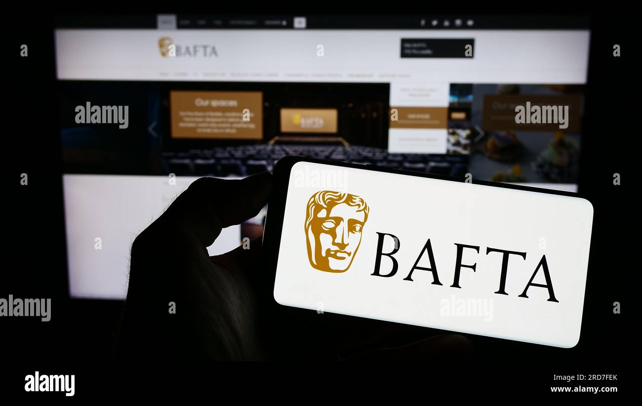 Persona in possesso di un cellulare con il logo dei British Academy Film Awards (BAFTA) sullo schermo davanti alla pagina web. Concentrarsi sul display del telefono. Foto Stock