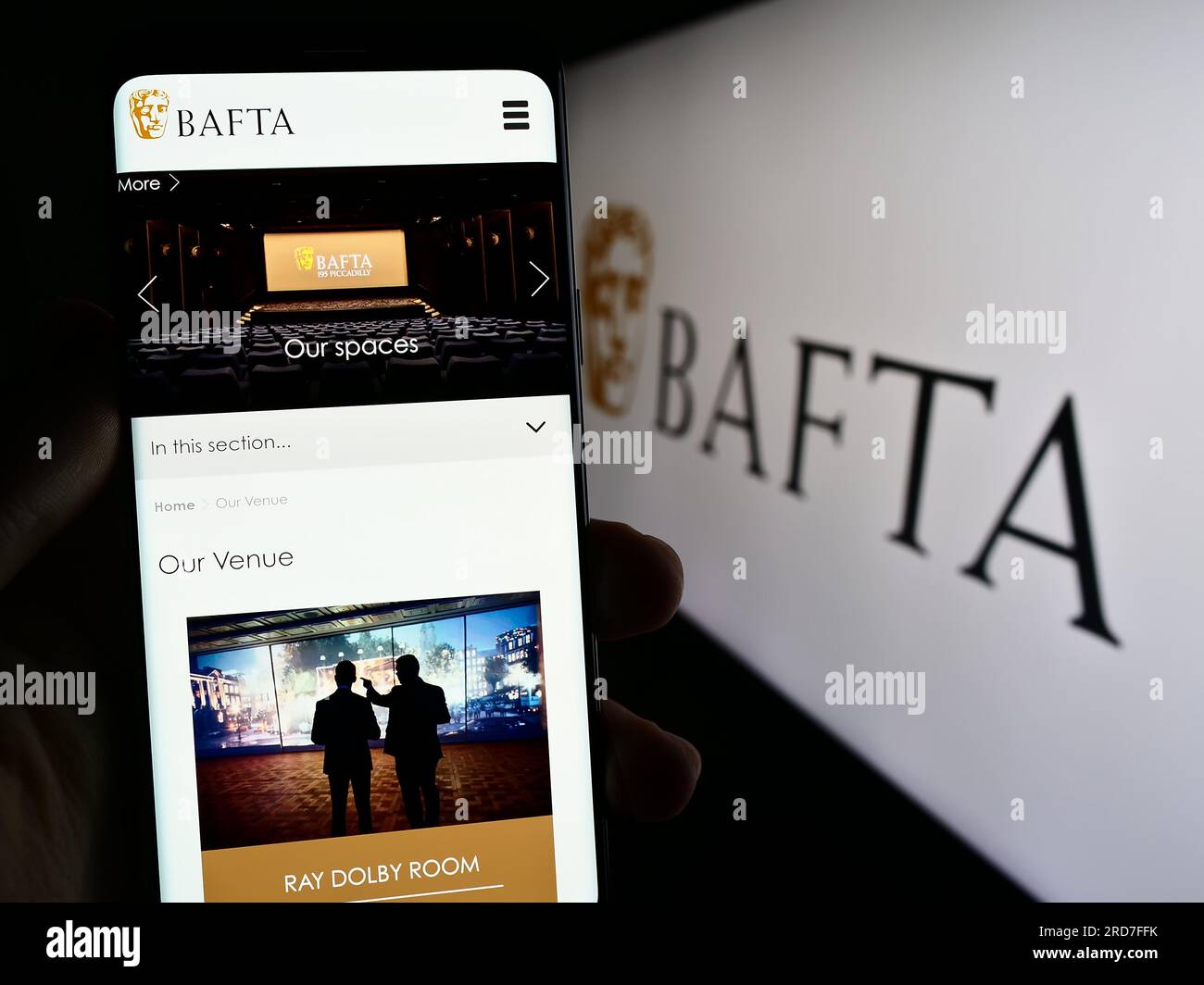 Persona che possiede uno smartphone con una pagina Web dei British Academy Film Awards (BAFTA) sullo schermo davanti al logo. Concentrarsi sul centro del display del telefono. Foto Stock