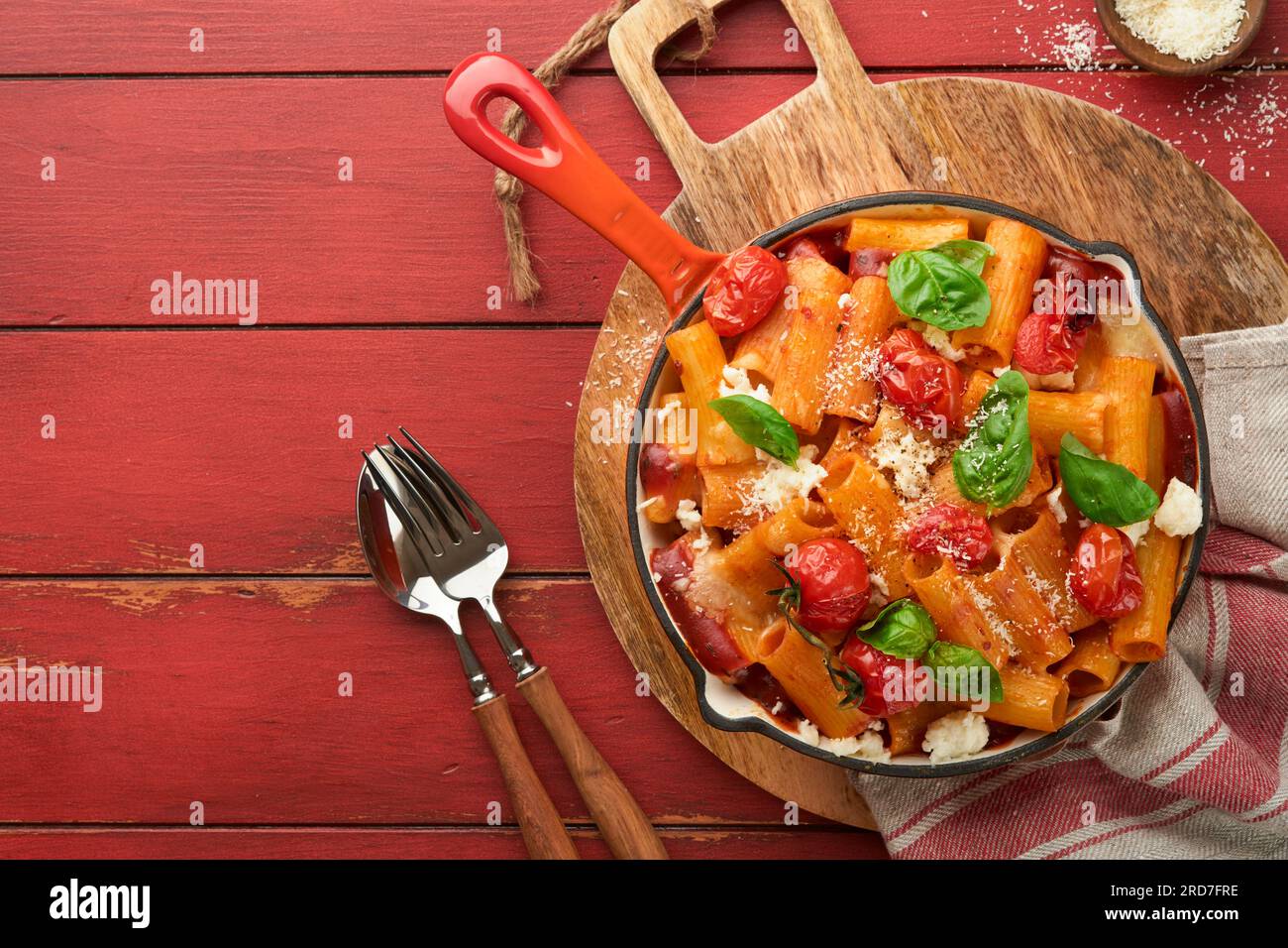 Tortiglioni di pasta con salsa di pomodoro, pomodori ciliegini al forno, mozzarella e parmigiano, basilico su vecchia tavola rustica rossa. Cucina tradizionale italiana Foto Stock