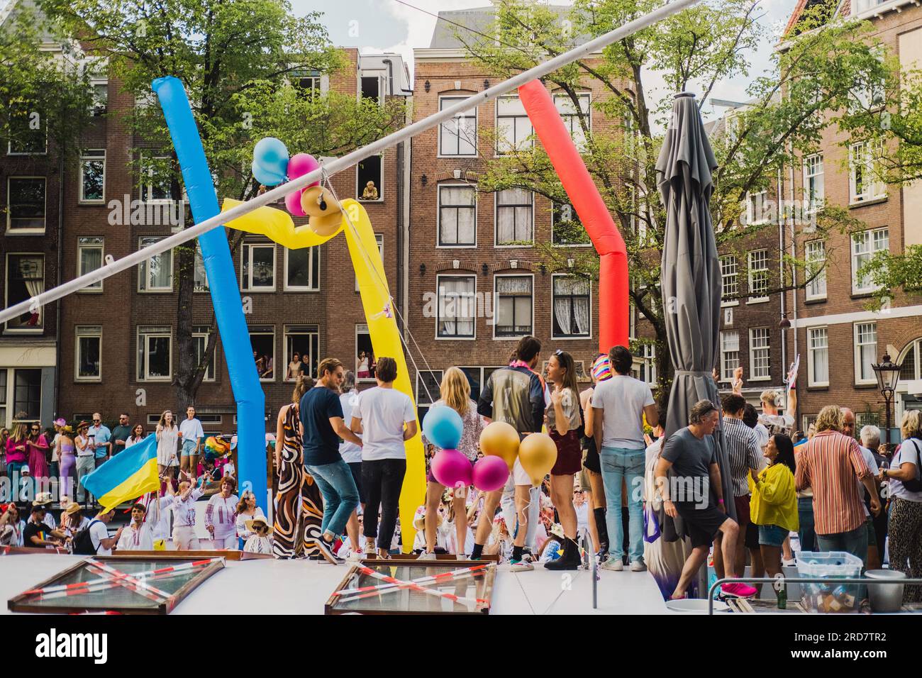 Amsterdam, Olanda settentrionale, Paesi Bassi – 6 agosto 2022: Una folla di persone in piedi su una casa galleggiante celebra il Pride Amsterdam circondato da una festa Foto Stock
