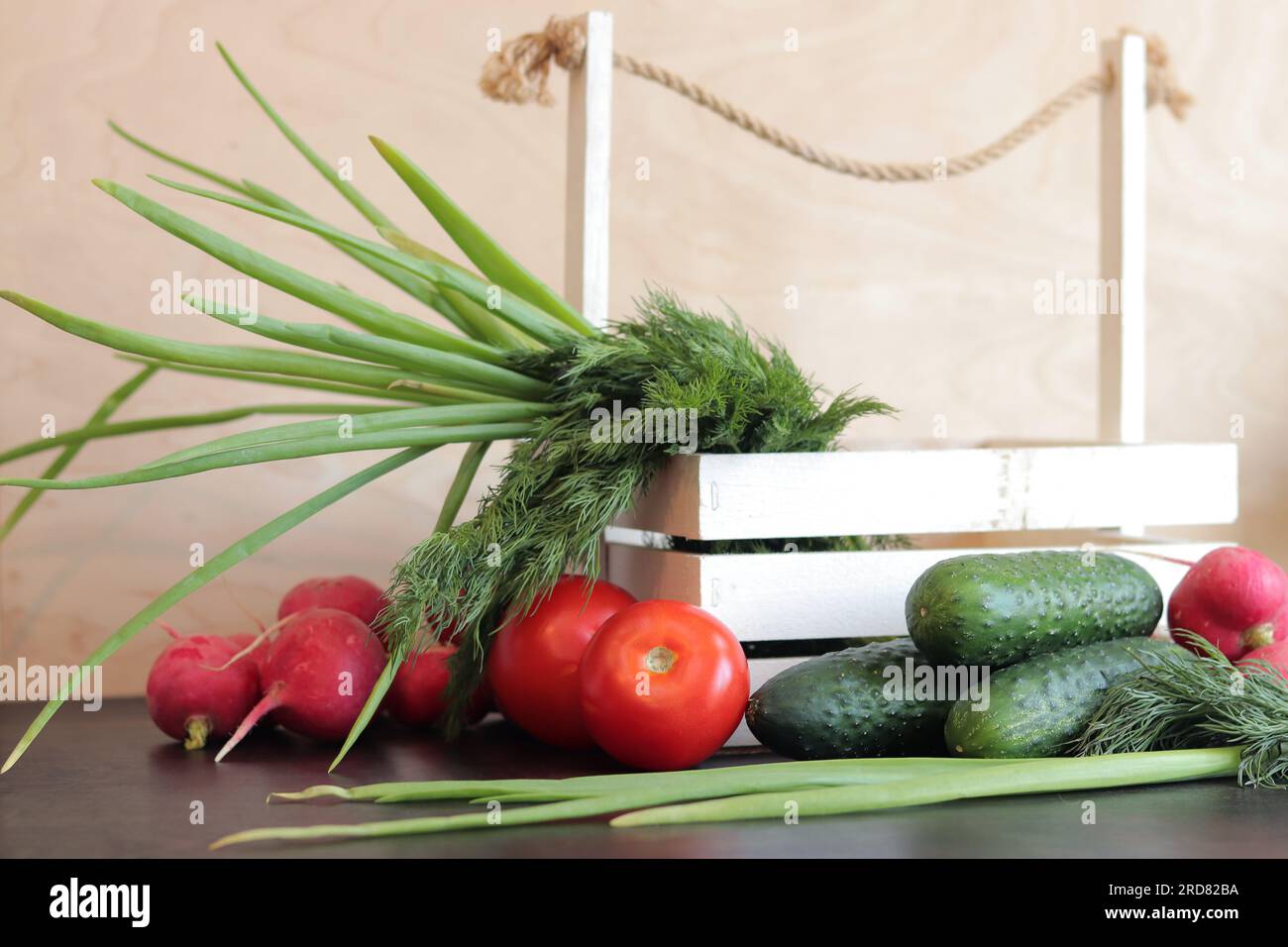 Cestino di legno con verdure fresche. Un mazzo di verdure fresche in un cestino su un tavolo di legno. Cetrioli, pomodori, ravanelli, cipolle verdi e aneto Foto Stock