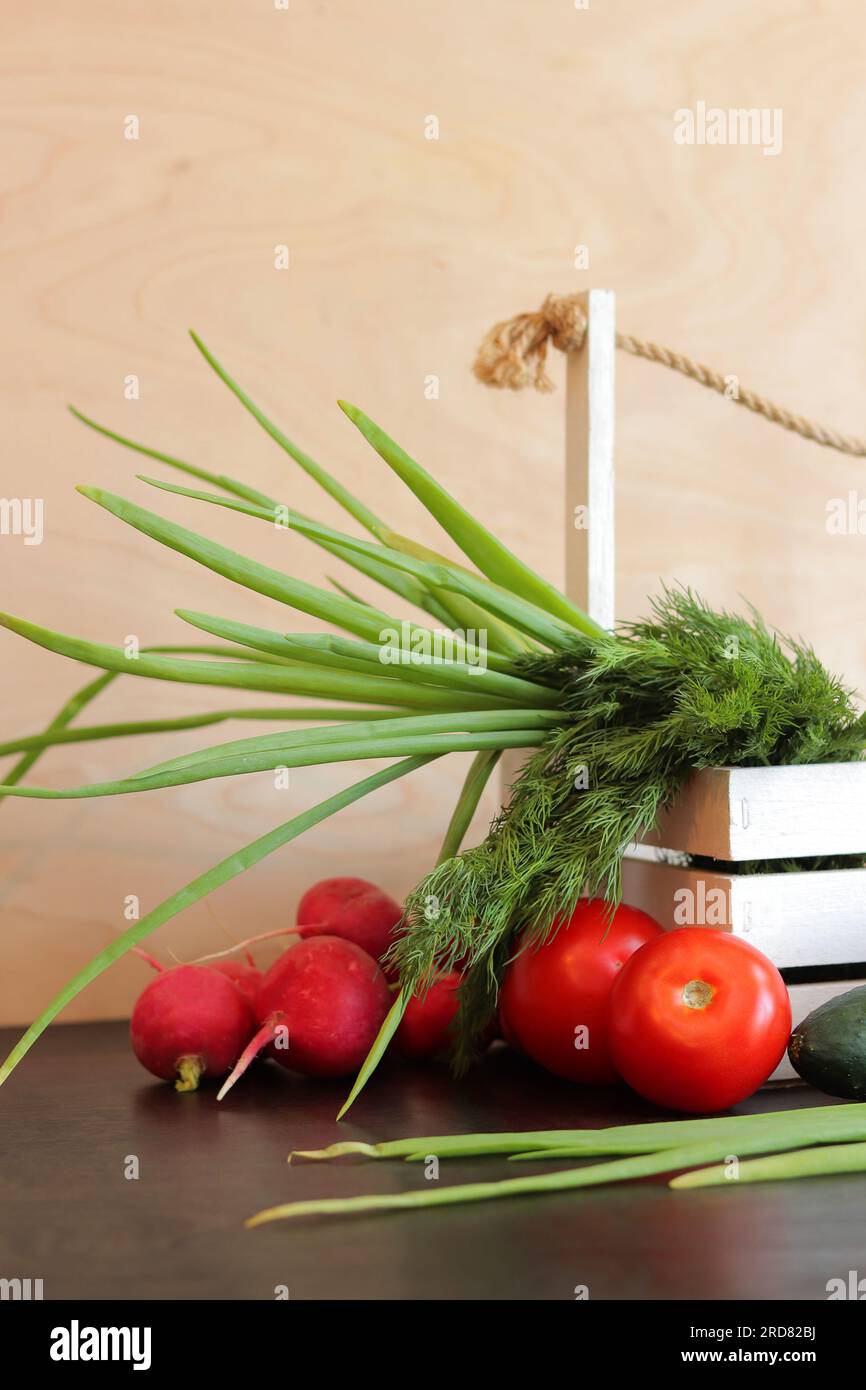 Cestino di legno con verdure fresche. Un mazzo di verdure in un cestino su un tavolo di legno. Cetrioli, pomodori, ravanelli, cipolle verdi e aneto Foto Stock