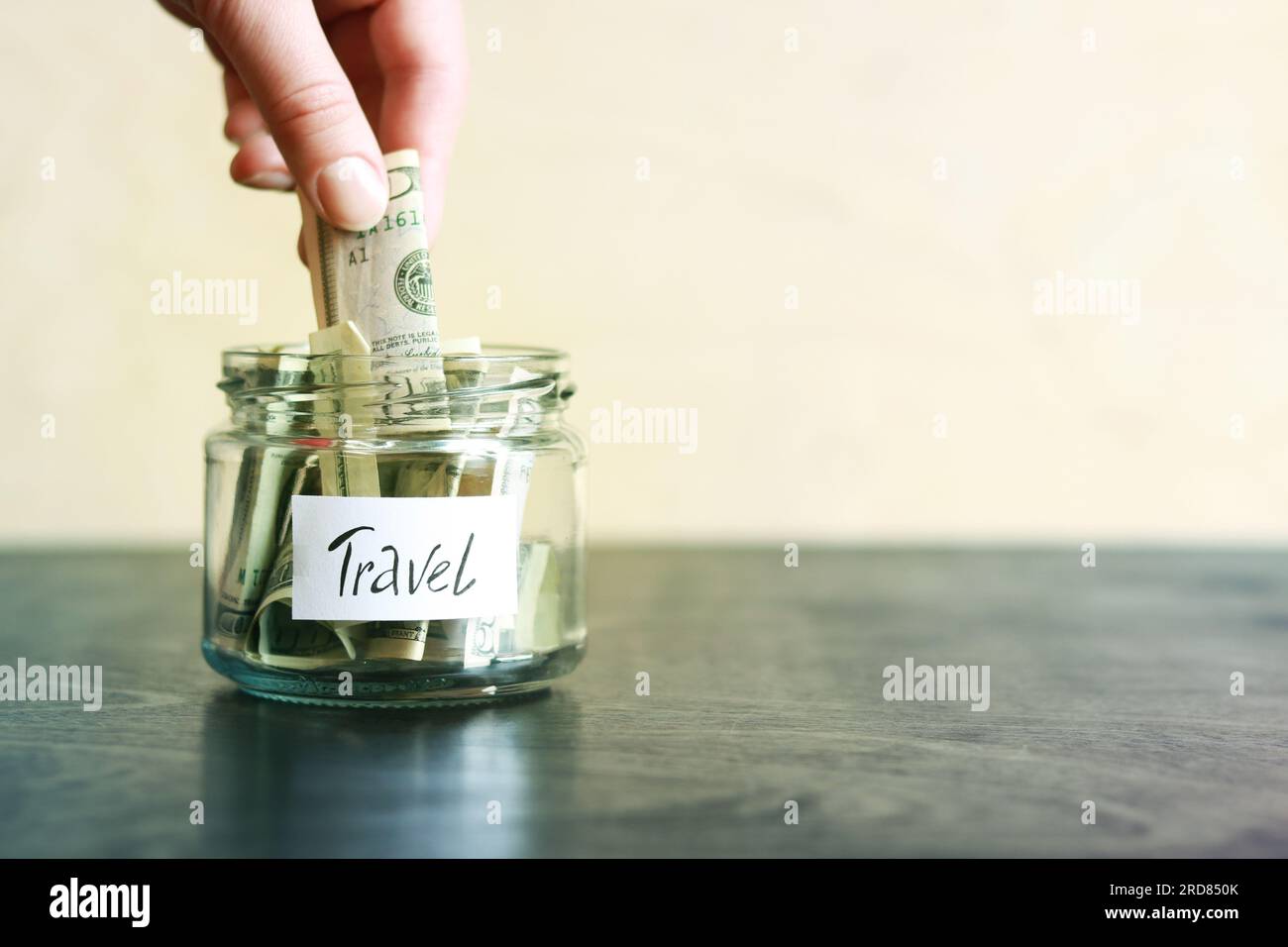 Salvadanaio con dollari per viaggiare. Vaso di vetro con soldi. La donna mette più soldi nel salvadanaio. Foto Stock