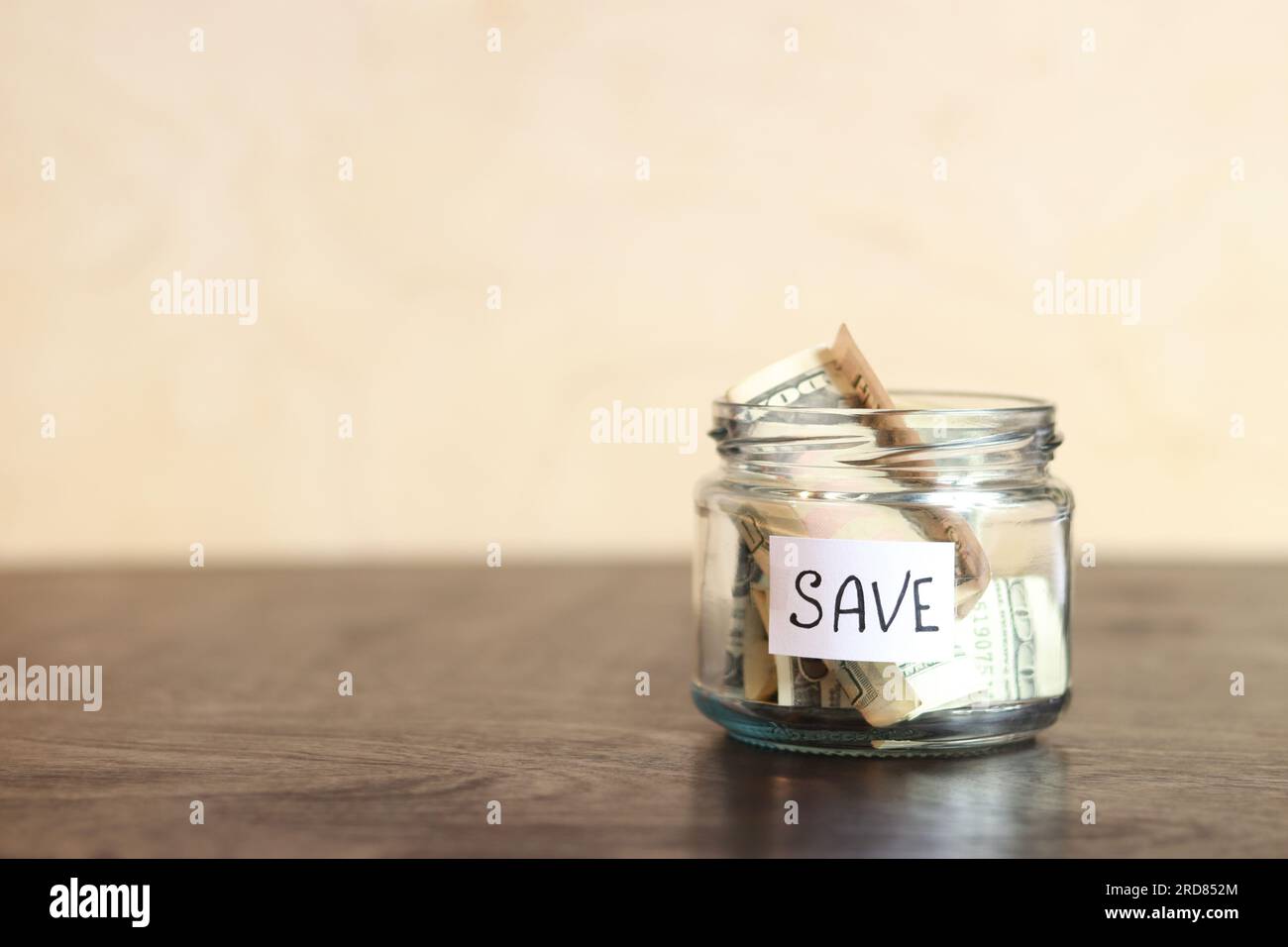 Risparmia denaro per il futuro. Vaso di vetro con dollari su un tavolo di legno. Salvadanaio con banconote, spazio per le copie. Il concetto di risparmio finanziario Foto Stock