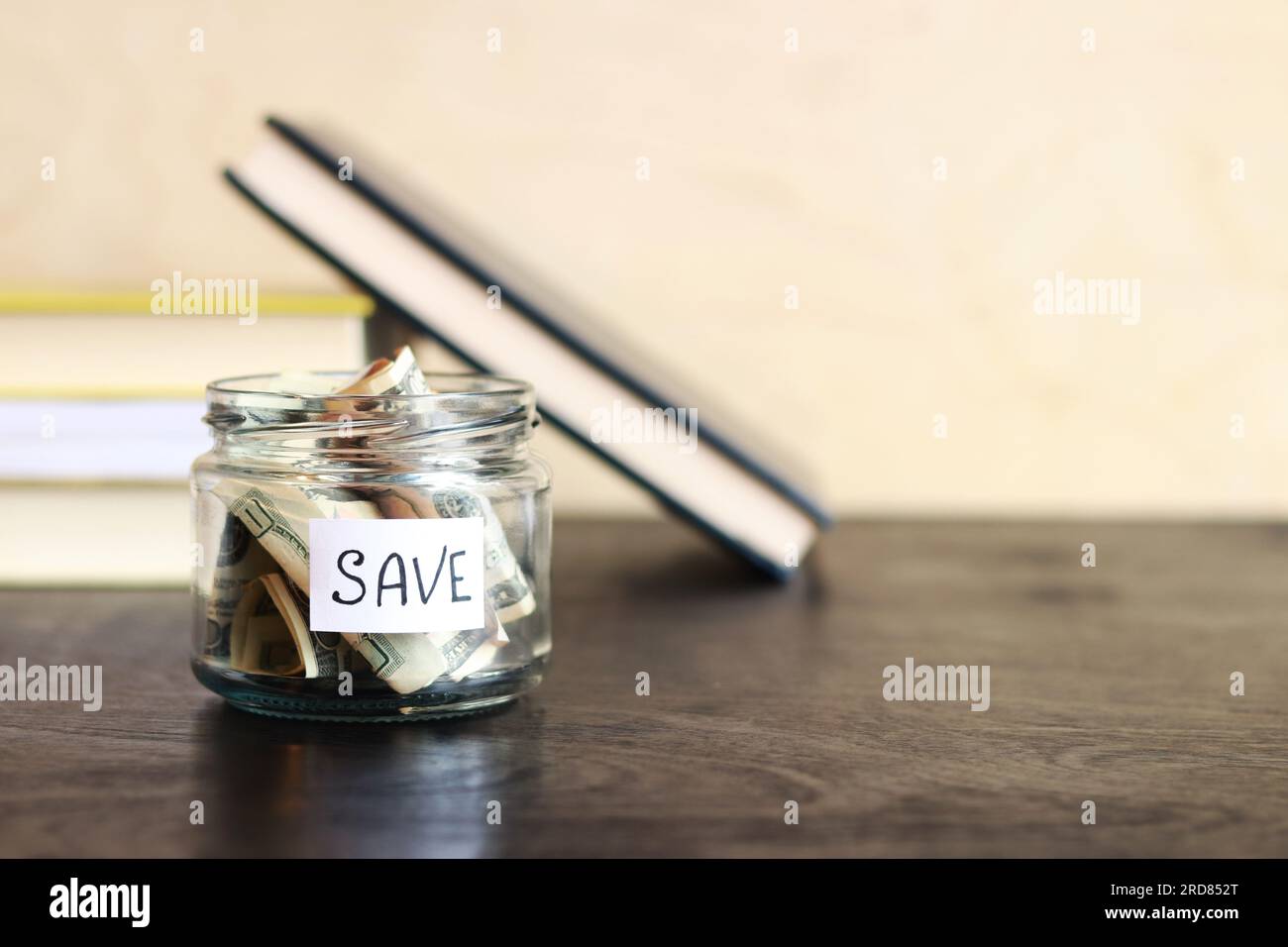 Risparmia denaro per il futuro. Vaso di vetro con dollari su un tavolo di legno sullo sfondo dei libri. Salvadanaio con banconote, spazio per le copie. Il concetto di Foto Stock