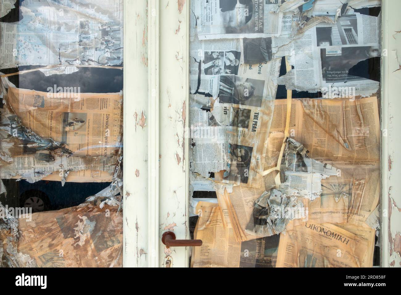 Una vetrata vuota e una porta coperta all'interno da un montaggio di giornali bloccati a caso, Cefalonia, Grecia Foto Stock