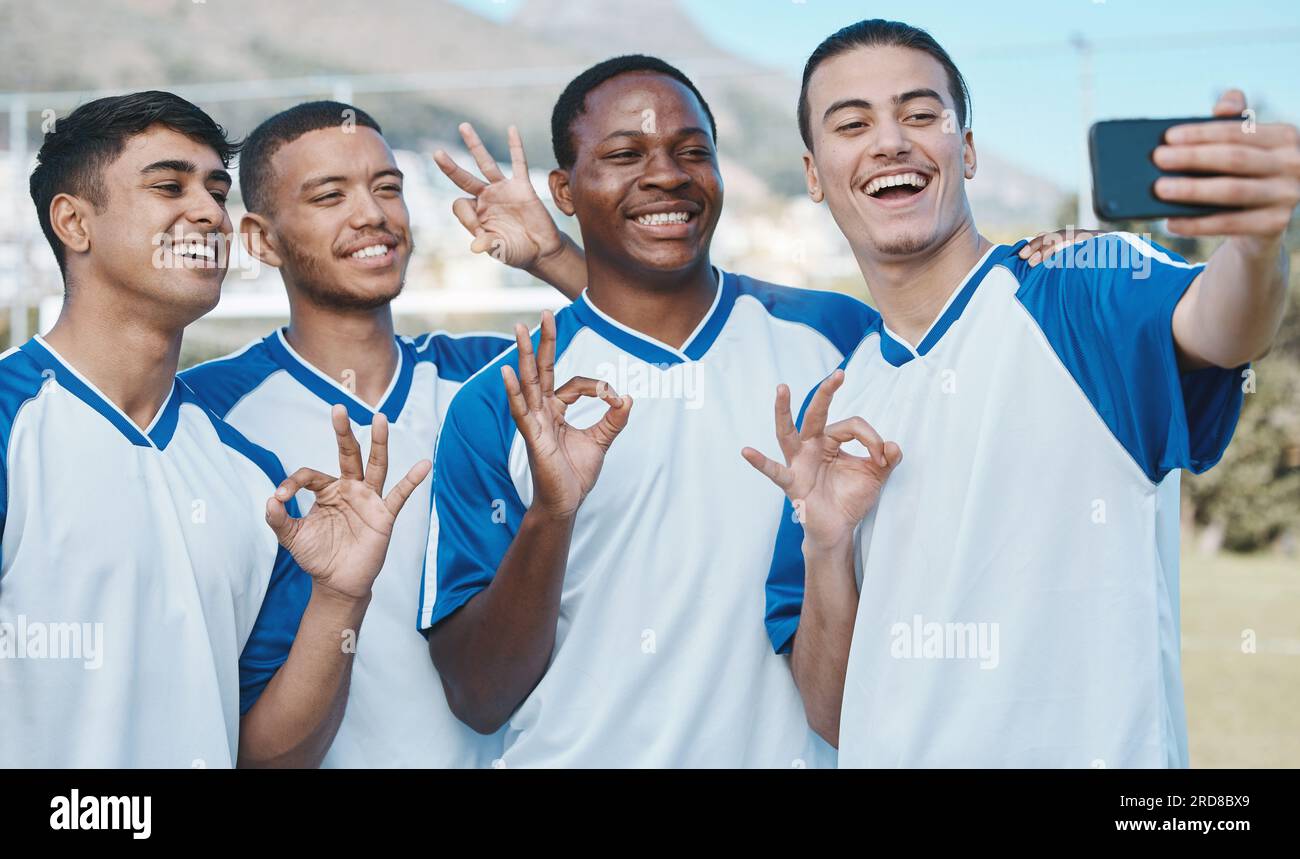 Uomini in selfie, OK mossa e competizione di calcio, sport e gruppo di atleti sul campo, diversità ed emoji. Felice, giovane giocatore di calcio maschile e squadra Foto Stock