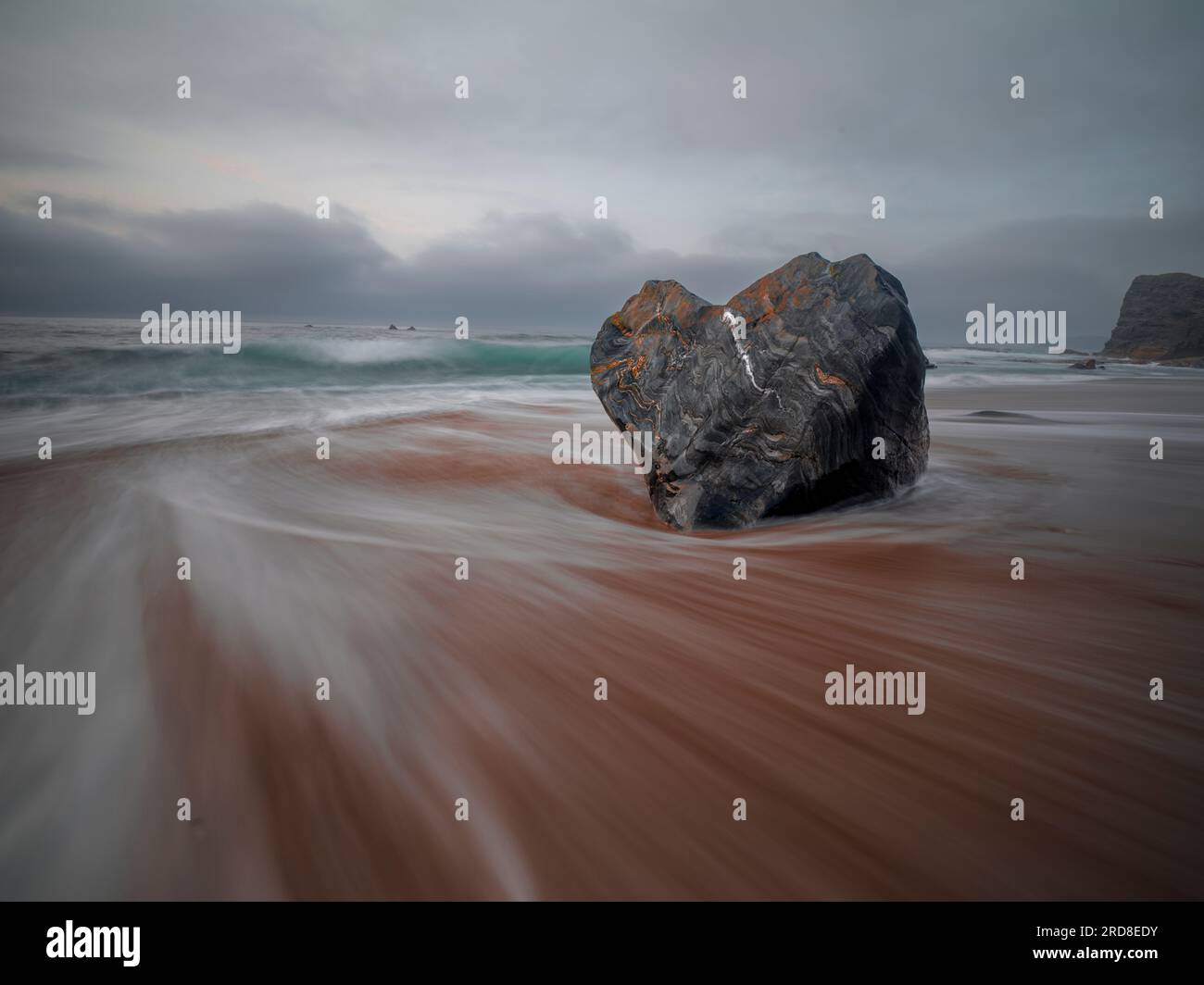 Lunga esposizione del mare che scorre e di una roccia a forma di cuore sulla spiaggia di Portizuelo, Asturie, Spagna, Europa Foto Stock