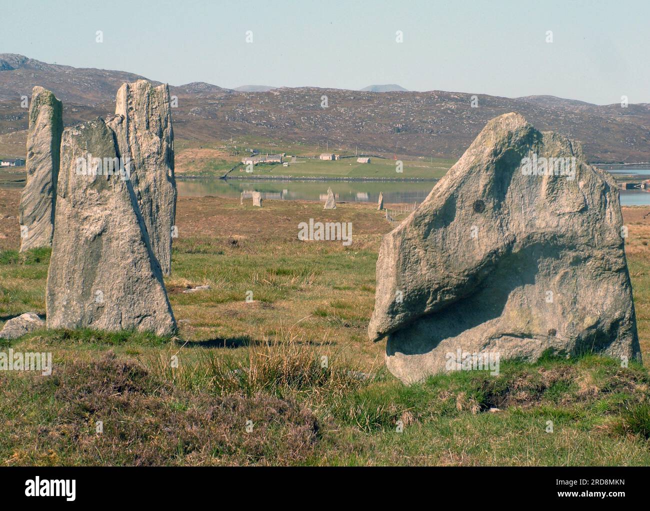 Pietre erette con le tranquille acque del Loch Ceann Huabhig e cottage sullo sfondo sulla costa occidentale dell'isola di Lewis nell'Hedr esterno Foto Stock