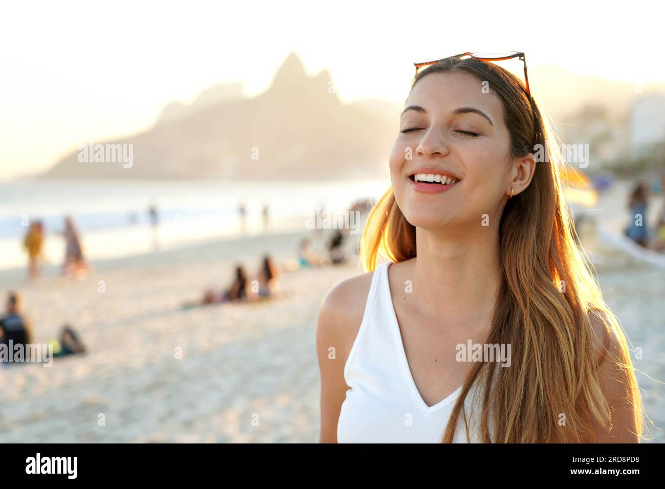 Ritratto di una giovane donna brasiliana sorridente a occhi chiusi sulla spiaggia di Ipanema al tramonto a Rio de Janeiro, Brasile Foto Stock