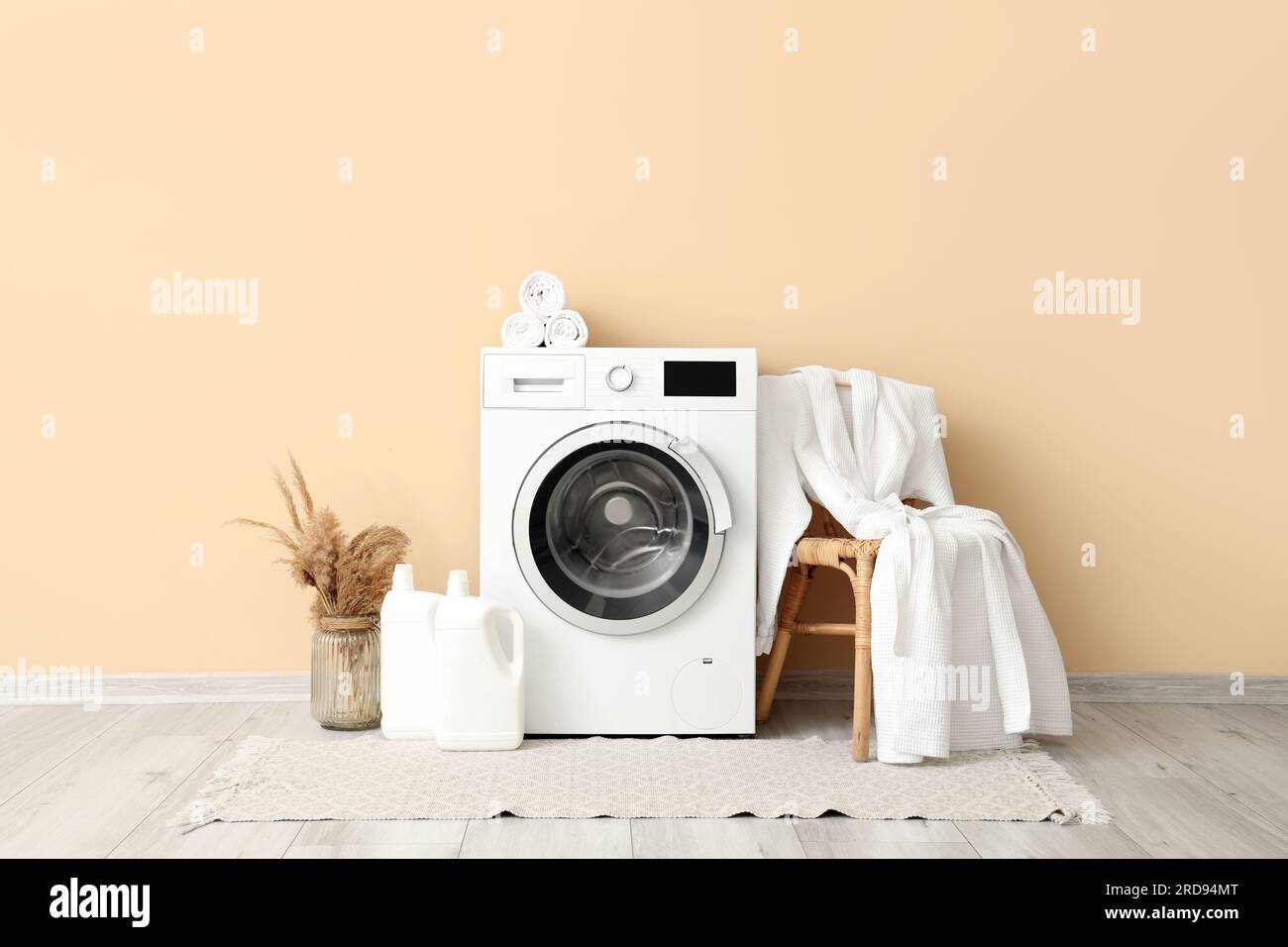 Lavatrice, sgabello con accappatoio e bottiglie di detergente vicino alle  pareti beige Foto stock - Alamy