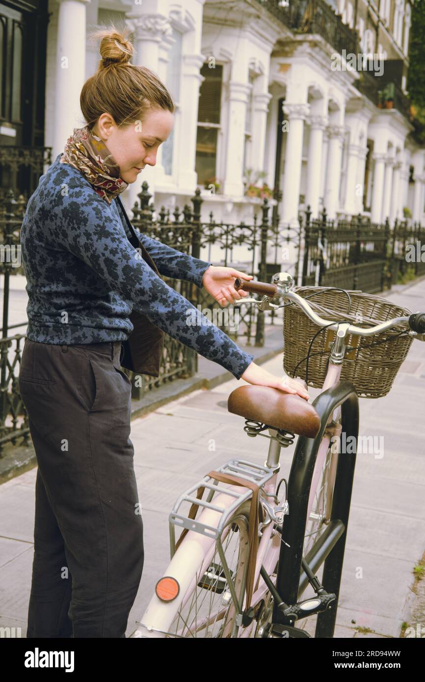 Giovane donna che prende la sua bicicletta rosa con un cesto e un campanello parcheggiato per la strada della città. Veicolo urbano non motorizzato senza emissione di carbonio Foto Stock