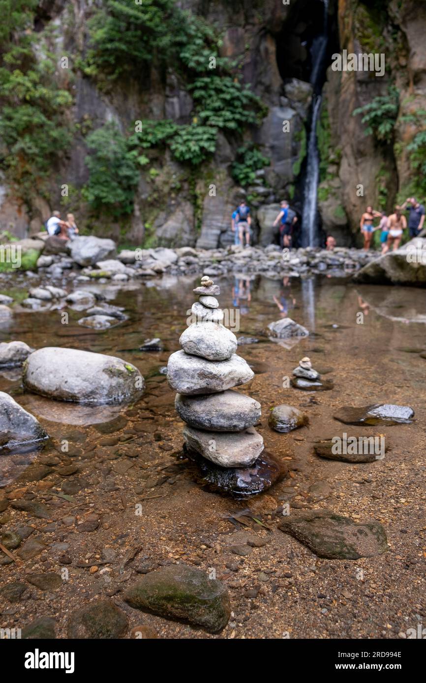 Un gruppo di zen pietre in un torrente circondato da turisti. Con la cascata del salto do Cabrito sullo sfondo. Isola di São Miguel nelle Azzorre Foto Stock