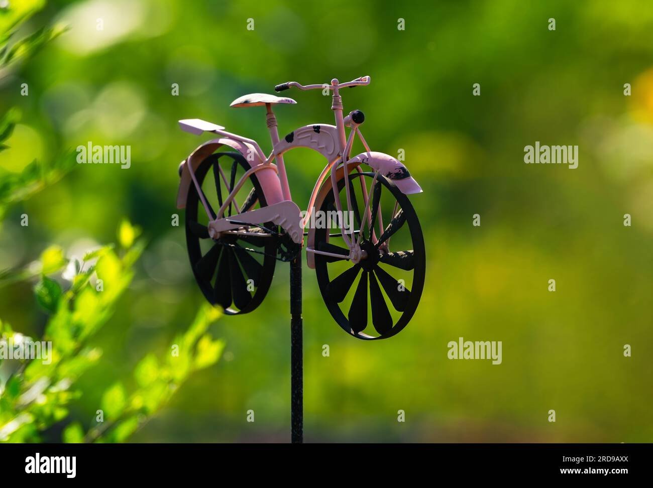 Una bizzarra bicicletta rosa su un palo aggiunge interesse decorativo a un giardino comunitario. Foto Stock