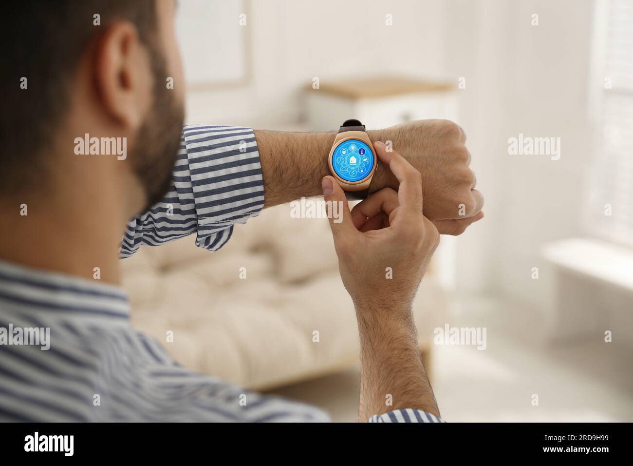 Uomo che imposta il sistema di controllo della casa intelligente tramite smartwatch al chiuso, primo piano. Interfaccia app con icone sul display Foto Stock
