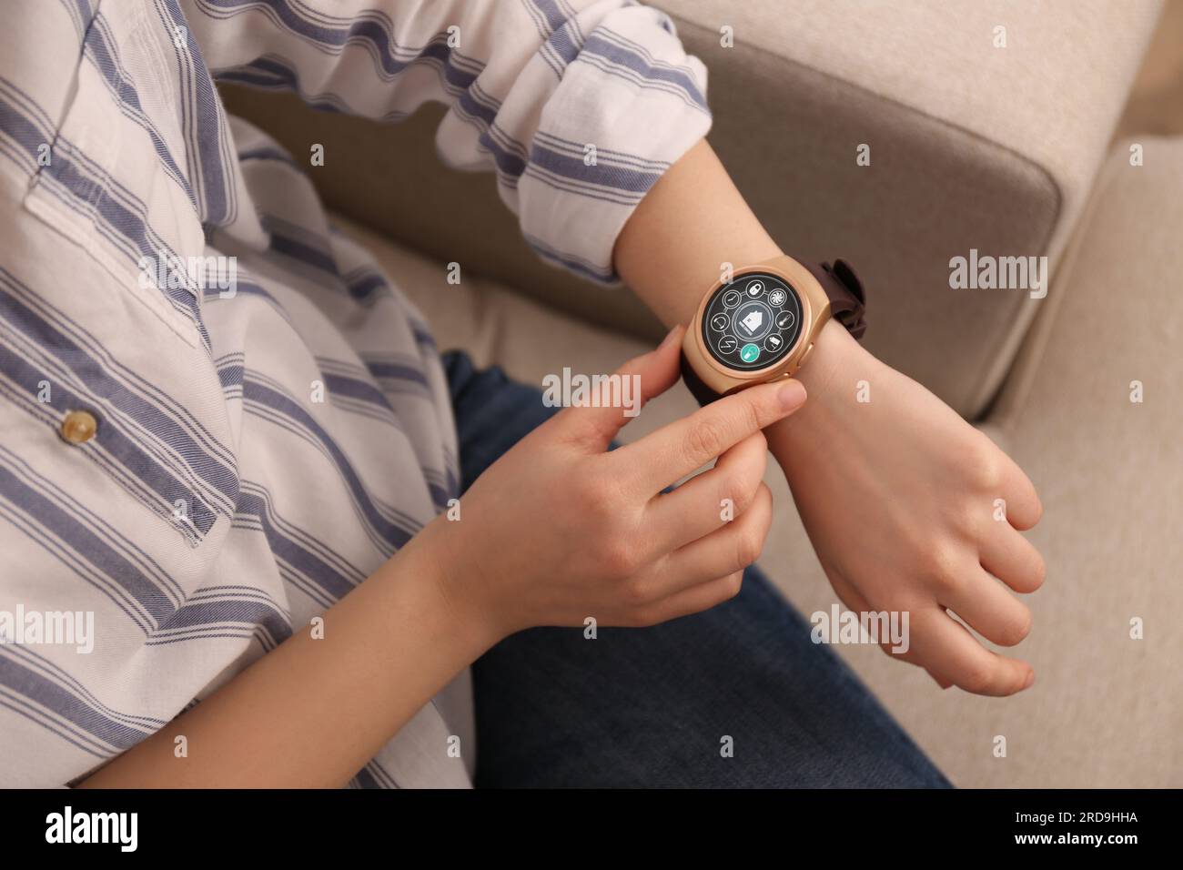 Donna che imposta il sistema di controllo della casa intelligente tramite smartwatch al chiuso, primo piano. Interfaccia app con icone sul display Foto Stock