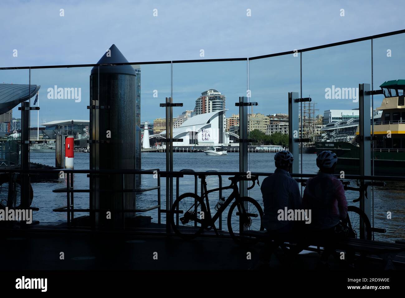 I pendolari guardano attraverso la parete di vetro sul molo dei traghetti a Barangaroo Sydney con Darling Harbour e Maritime Museum sullo sfondo Foto Stock