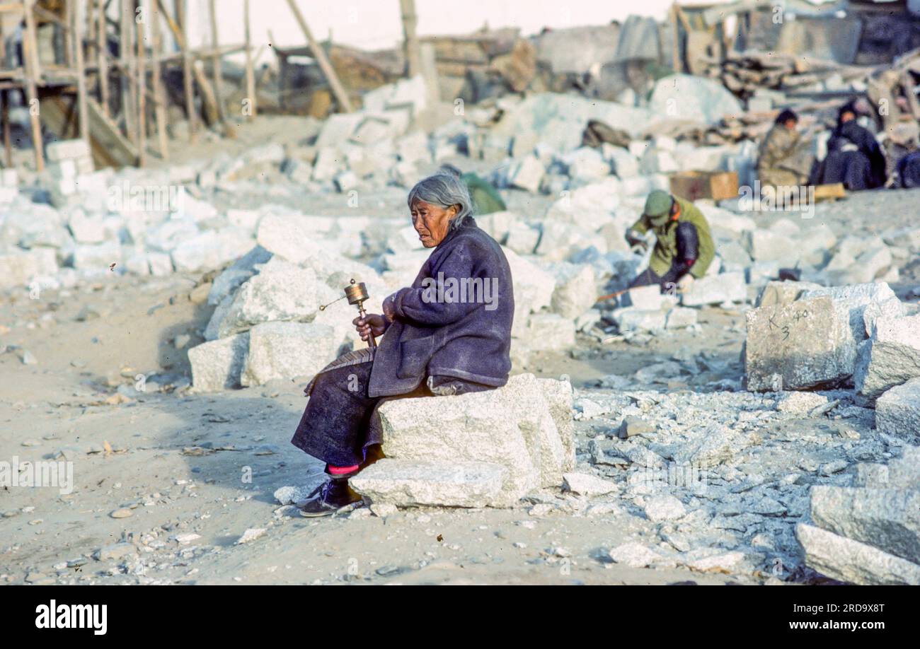 Lhasa, Cina - 19 aprile 1987: Ritratto di una vecchia donna locale dalle colline usando la ruota di preghiera a Lhasa, Cina, seduto nel cantiere di Foto Stock