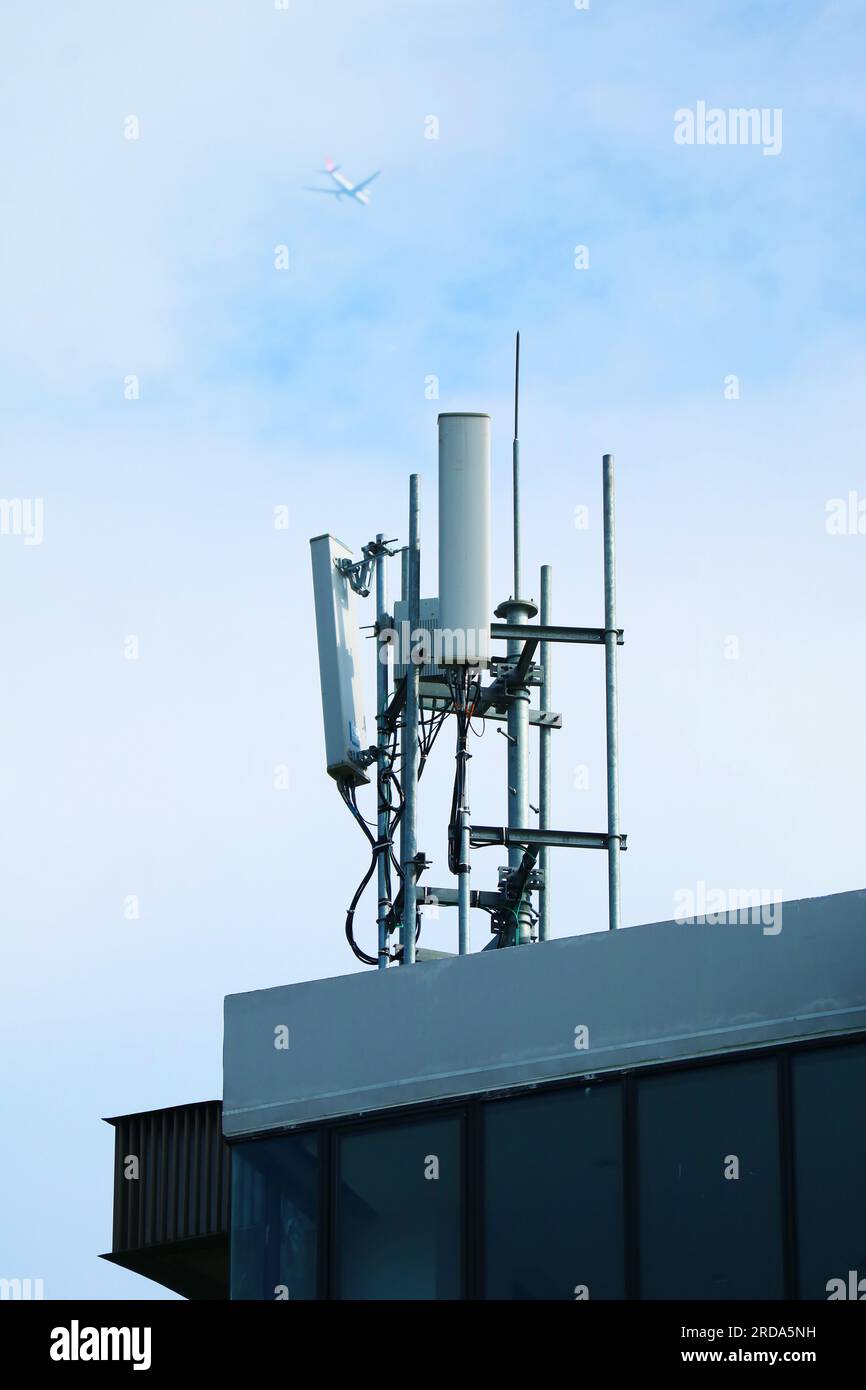 Antenne per telefoni cellulari sul tetto con aereo in volo su cielo nuvoloso Foto Stock
