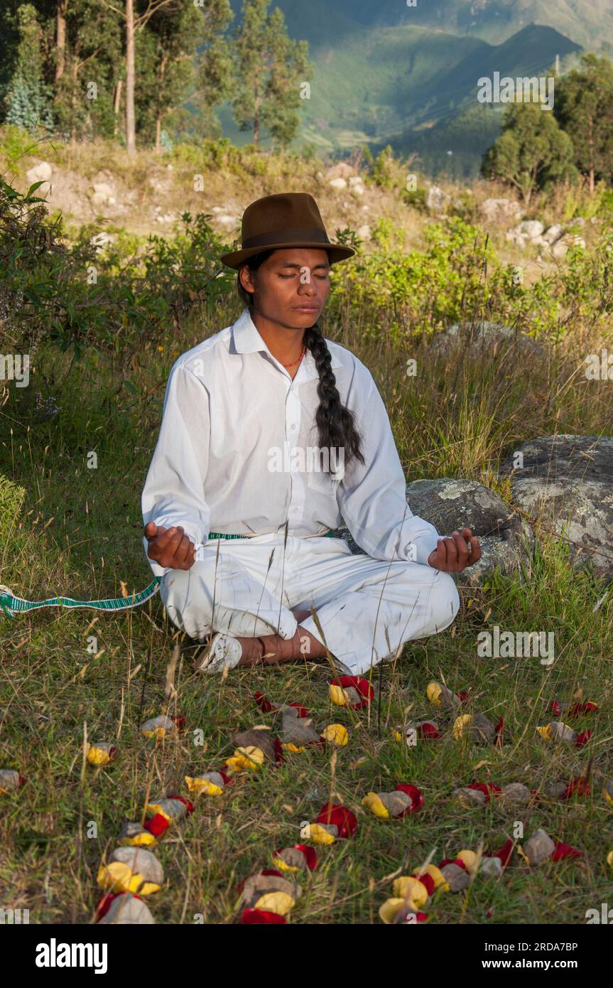 uomo indigeno di otavalo che medita accanto a una figura ancestrale fatta di petali di rosa e pietre Foto Stock