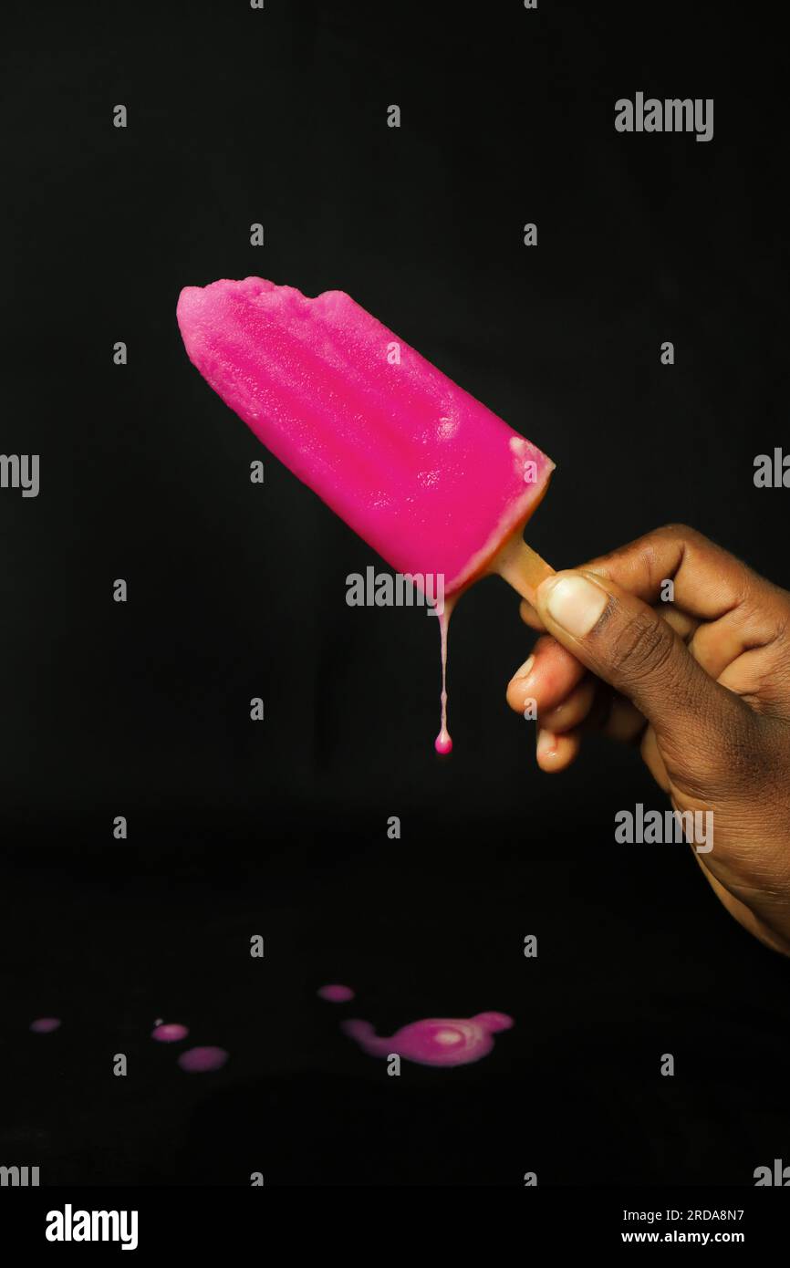 Gelato rosa su un bastoncino su sfondo nero, vista frontale Foto Stock