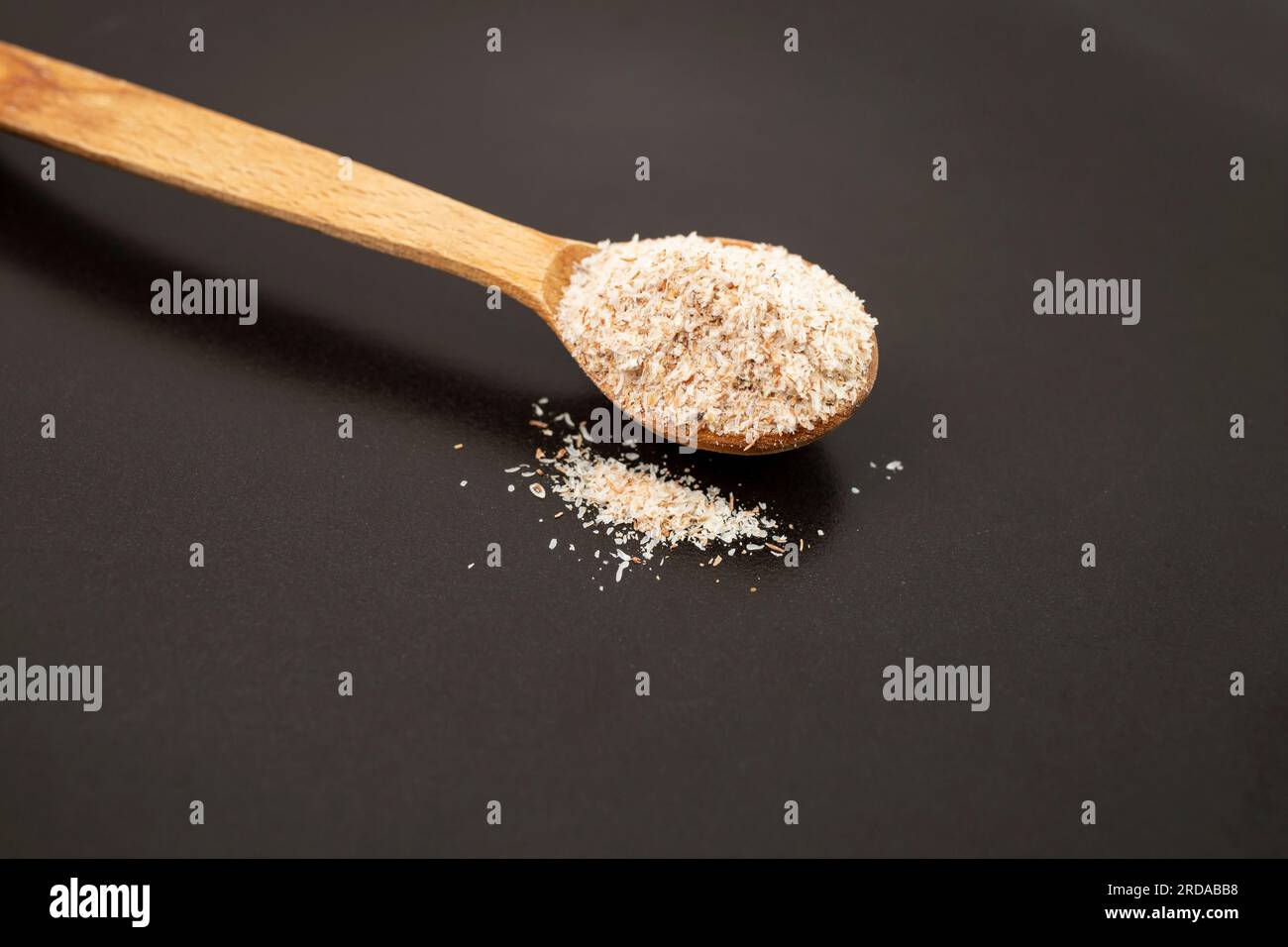 Cucchiaino di legno pieno di psicllio su piastra di ceramica nera, medicina alternativa per disfunzioni digestive Foto Stock