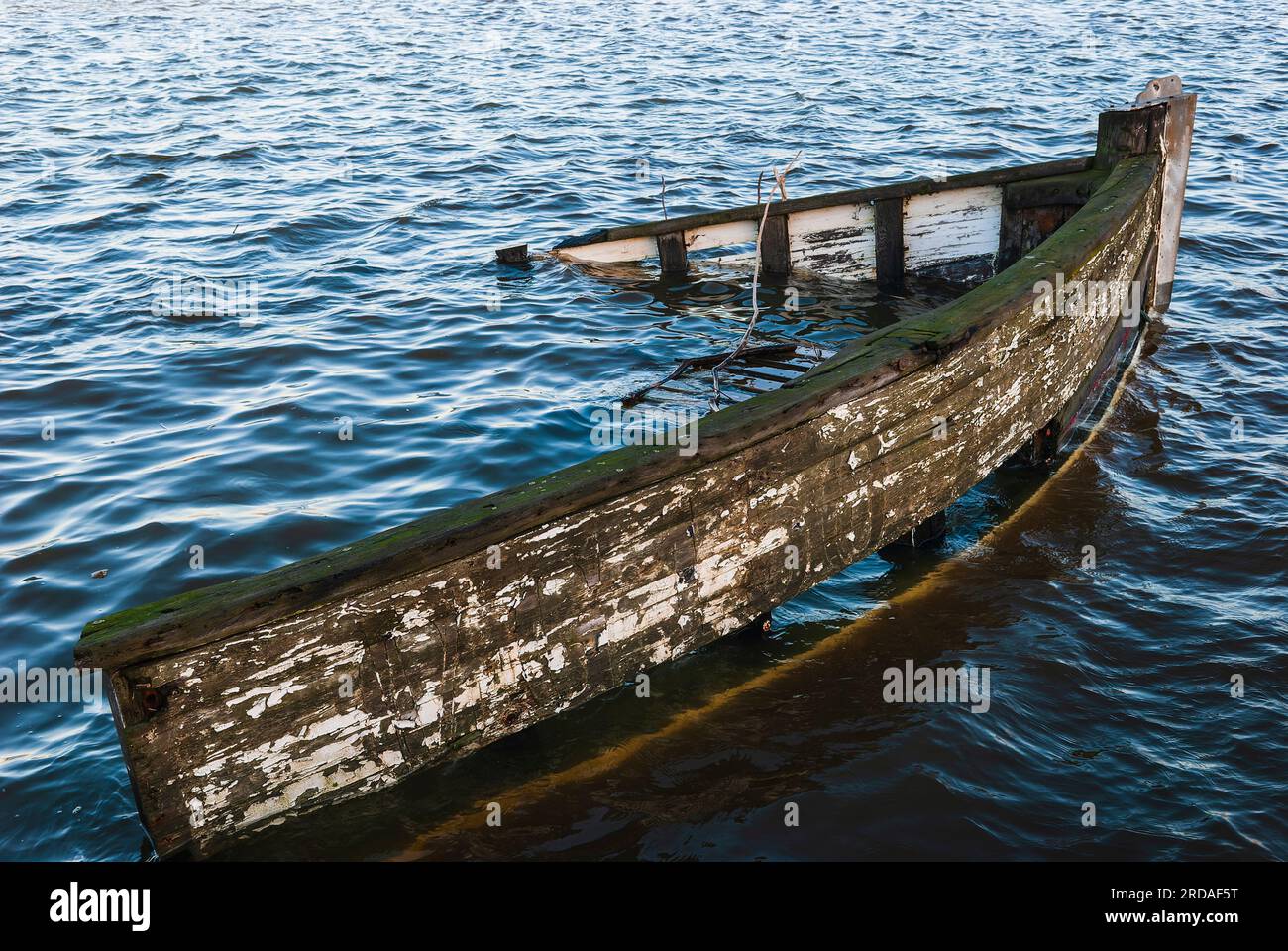 Un relitto di una nave affondata riposa sul fondo di un tranquillo porto, il suo scafo scintillante nel mare illuminato dal sole. Foto Stock