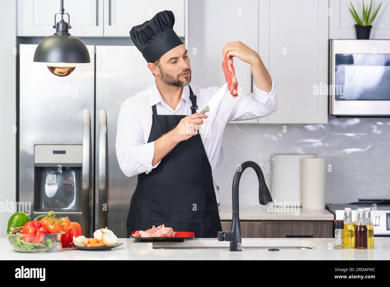 Uomo in grembiule e cappello da chef cucinare cibo in cucina. Bell'uomo che  cucina cibi