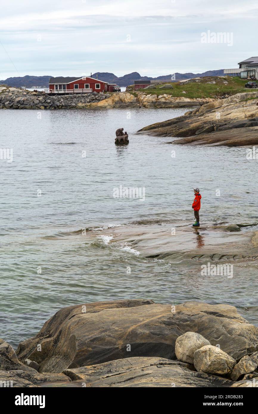 Donna in piedi su rocce che guarda la madre del mare, Sassuma Arnaa, scultura di Christian Rosing a Nuuk, Groenlandia, a luglio Foto Stock