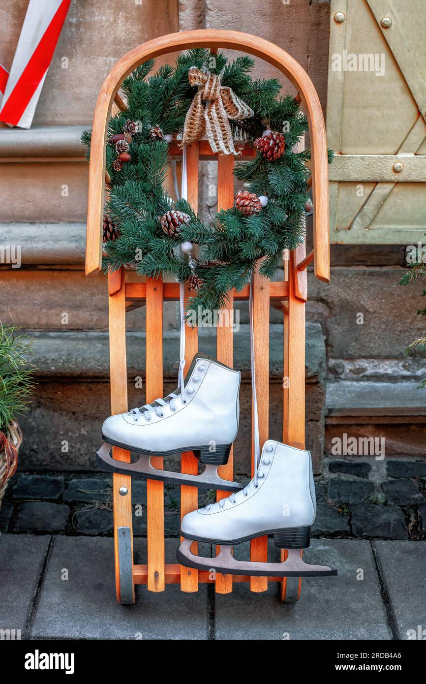 Due pattini di ghiaccio a figura, slitta di legno, corona di Natale . Abbina scarpe da skate in pelle bianca appese, decorazioni in slitta di legno con corona di abete. Inverno vintage Foto Stock