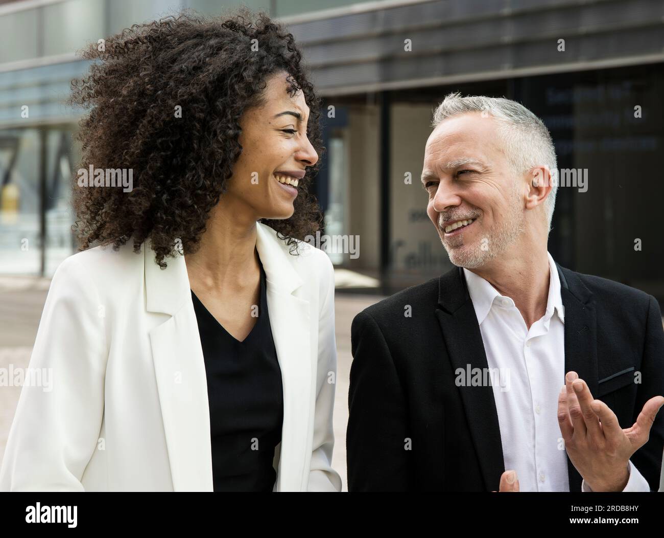 Donna d'affari e uomo d'affari che parlano e sorridono per strada. Incontro informale tra un giovane dirigente e un ceo senior che si diverte all'aperto. Foto Stock