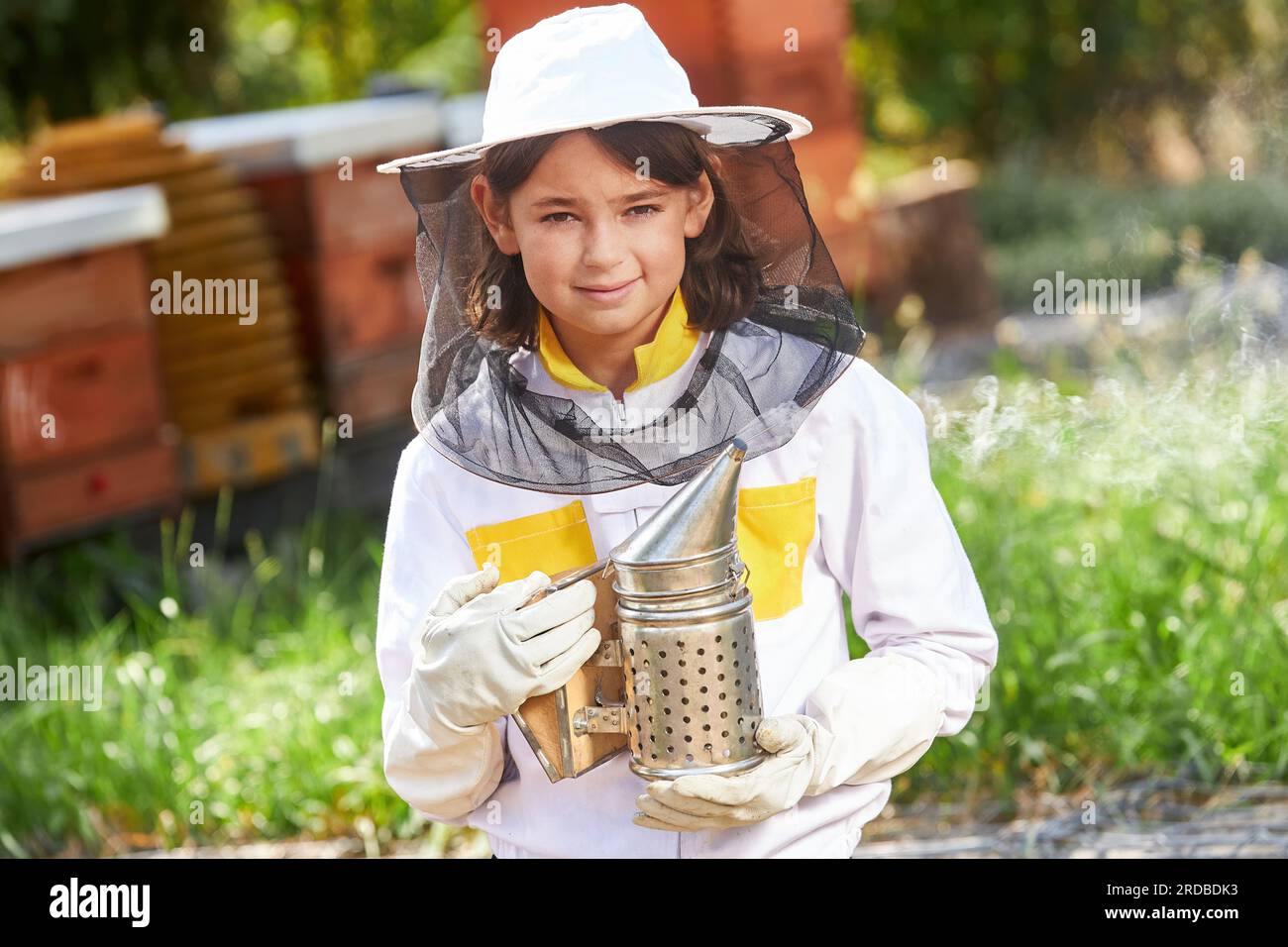 Ritratto di una ragazza sorridente che tiene un fumatore che emette fumo in piedi nel giardino dell'apiario Foto Stock