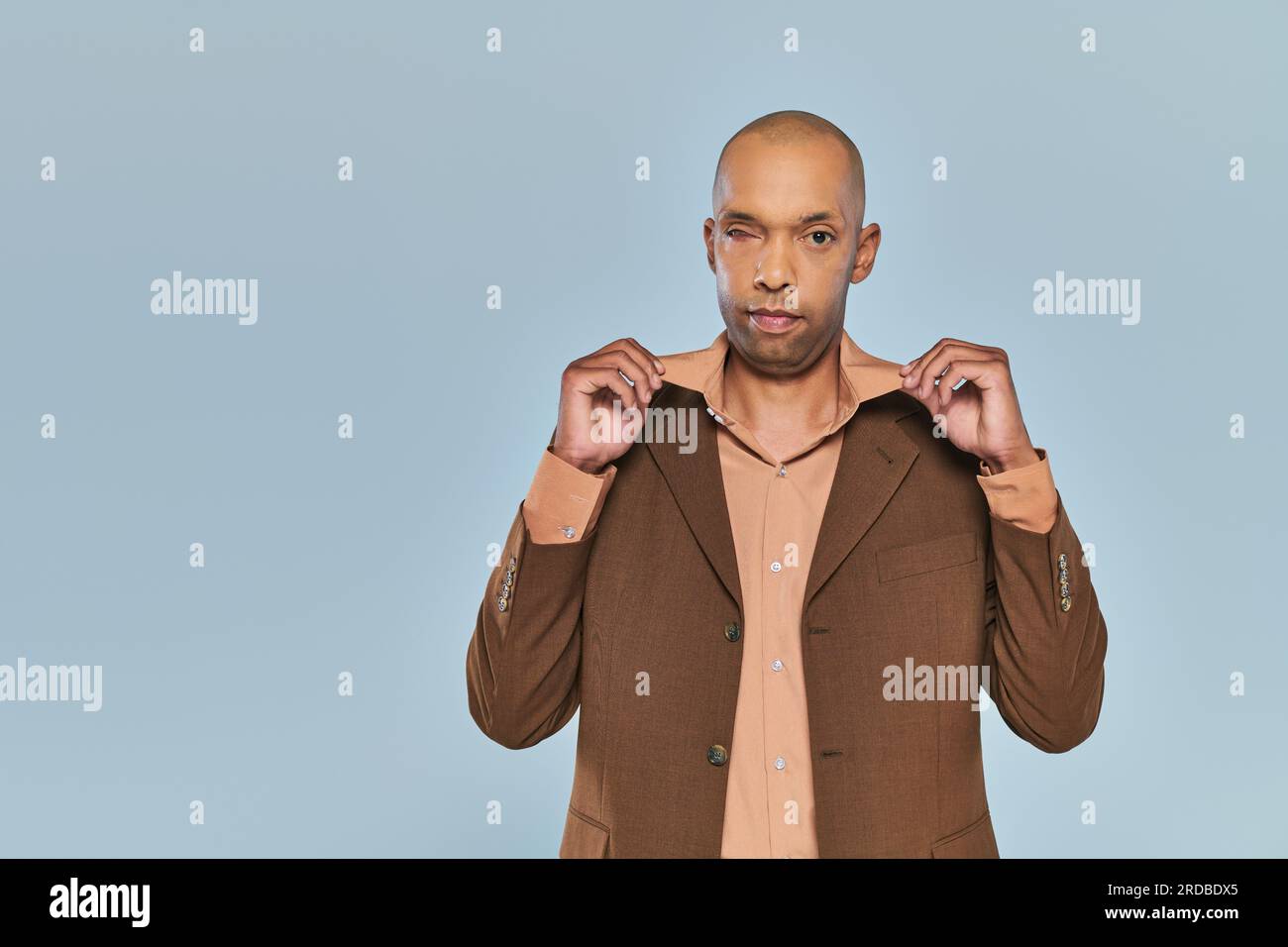 sindrome oculare, compromissione fisica, audace uomo afro-americano con miastenia gravis in piedi su sfondo grigio, persona dalla pelle scura in stile formale Foto Stock