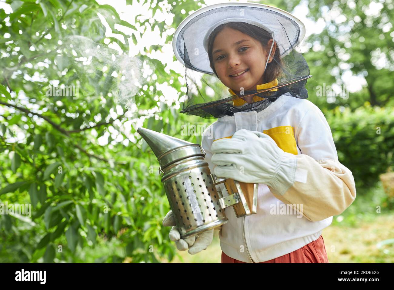 Ritratto di una ragazza sorridente che tiene un fumatore in piedi nel giardino dell'apiario Foto Stock