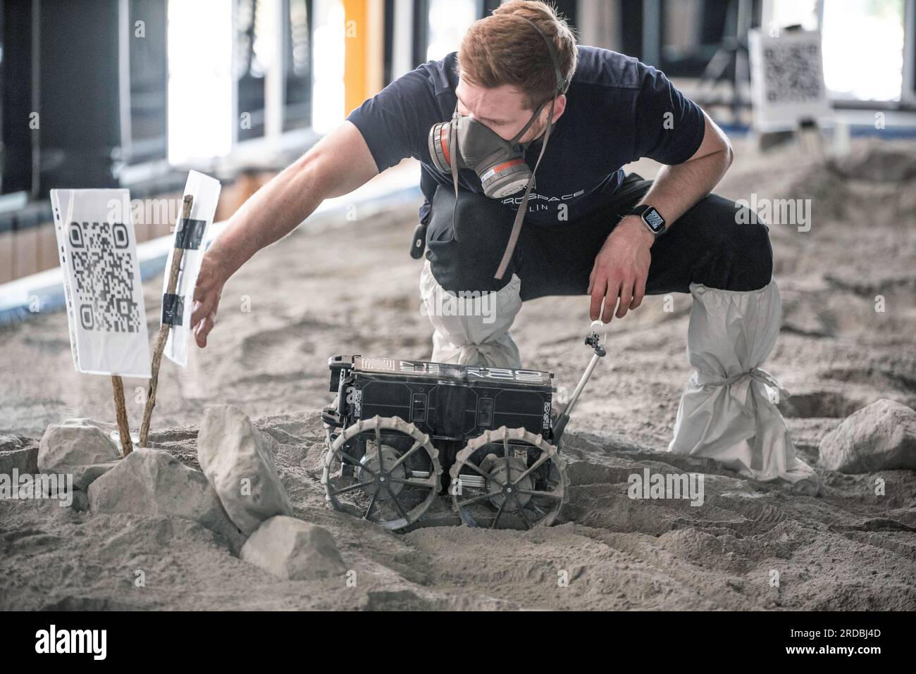 20 luglio 2023, Meclemburgo-Pomerania Occidentale, Rostock-Laage: L'ingegnere di sviluppo Max Manthey della Neurospace GmbH crea un cartello con un codice QR per i rover di prova del Neurospace in un campo di test nel terminal aeroportuale dell'aeroporto di Rostock-Laage. Il letto lunare costruito artificialmente nel terminal dell'aeroporto è lungo circa 18 metri, largo cinque metri e pieno di "polvere lunare" sulla superficie. Per celebrare la giornata internazionale della Luna in commemorazione del primo atterraggio con equipaggio il 20 luglio 1969, i piccoli rover di prova stanno ancora una volta arando attraverso un paesaggio lunare creato artificialmente all'aeroporto di Rostock-Laage tod Foto Stock 20 luglio 2023, Meclemburgo-Pomerania Occidentale, Rostock-Laage: L'ingegnere di sviluppo Max Manthey della Neurospace GmbH crea un cartello con un codice QR per i rover di prova del Neurospace in un campo di test nel terminal aeroportuale dell'aeroporto di Rostock-Laage. Il letto lunare costruito artificialmente nel terminal dell'aeroporto è lungo circa 18 metri, largo cinque metri e pieno di "polvere lunare" sulla superficie. Per celebrare la giornata internazionale della Luna in commemorazione del primo atterraggio con equipaggio il 20 luglio 1969, i piccoli rover di prova stanno ancora una volta arando attraverso un paesaggio lunare creato artificialmente all'aeroporto di Rostock-Laage tod Foto Stock