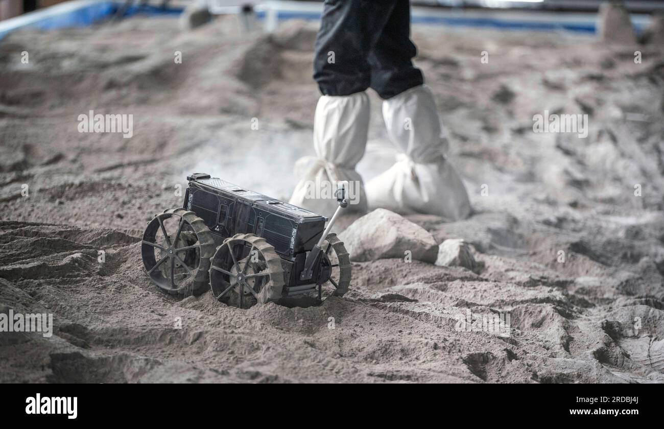 20 luglio 2023, Meclemburgo-Pomerania occidentale, Rostock-Laage: L'ingegnere di sviluppo Max Manthey della Neurospace GmbH accompagna il viaggio di un rover lunare su un campo di prova nel terminal aeroportuale dell'aeroporto di Rostock-Laage. Il letto lunare costruito artificialmente nel terminal dell'aeroporto è lungo circa 18 metri, largo cinque metri e pieno di "polvere lunare" sulla superficie. In occasione della giornata internazionale della Luna che celebra il primo atterraggio con equipaggio il 20 luglio 1969, i piccoli rover di prova stanno ancora arando attraverso un paesaggio lunare creato artificialmente all'aeroporto di Rostock-Laage. Foto: Frank Foto Stock 20 luglio 2023, Meclemburgo-Pomerania occidentale, Rostock-Laage: L'ingegnere di sviluppo Max Manthey della Neurospace GmbH accompagna il viaggio di un rover lunare su un campo di prova nel terminal aeroportuale dell'aeroporto di Rostock-Laage. Il letto lunare costruito artificialmente nel terminal dell'aeroporto è lungo circa 18 metri, largo cinque metri e pieno di "polvere lunare" sulla superficie. In occasione della giornata internazionale della Luna che celebra il primo atterraggio con equipaggio il 20 luglio 1969, i piccoli rover di prova stanno ancora arando attraverso un paesaggio lunare creato artificialmente all'aeroporto di Rostock-Laage. Foto: Frank Foto Stock