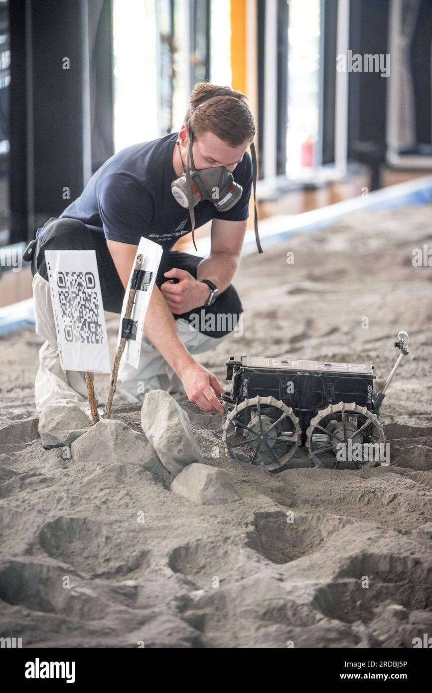 20 luglio 2023, Meclemburgo-Pomerania Occidentale, Rostock-Laage: L'ingegnere di sviluppo Max Manthey della Neurospace GmbH installa un rover lunare per un giro su un campo di prova nel terminal dell'aeroporto di Rostock-Laage. Il letto lunare costruito artificialmente nel terminal dell'aeroporto è lungo circa 18 metri, largo cinque metri e pieno di "polvere lunare" sulla superficie. In occasione della giornata internazionale della Luna che celebra il primo atterraggio con equipaggio il 20 luglio 1969, i piccoli rover di prova stanno ancora arando attraverso un paesaggio lunare creato artificialmente all'aeroporto di Rostock-Laage. Foto: Frank Horman Foto Stock 20 luglio 2023, Meclemburgo-Pomerania Occidentale, Rostock-Laage: L'ingegnere di sviluppo Max Manthey della Neurospace GmbH installa un rover lunare per un giro su un campo di prova nel terminal dell'aeroporto di Rostock-Laage. Il letto lunare costruito artificialmente nel terminal dell'aeroporto è lungo circa 18 metri, largo cinque metri e pieno di "polvere lunare" sulla superficie. In occasione della giornata internazionale della Luna che celebra il primo atterraggio con equipaggio il 20 luglio 1969, i piccoli rover di prova stanno ancora arando attraverso un paesaggio lunare creato artificialmente all'aeroporto di Rostock-Laage. Foto: Frank Horman Foto Stock