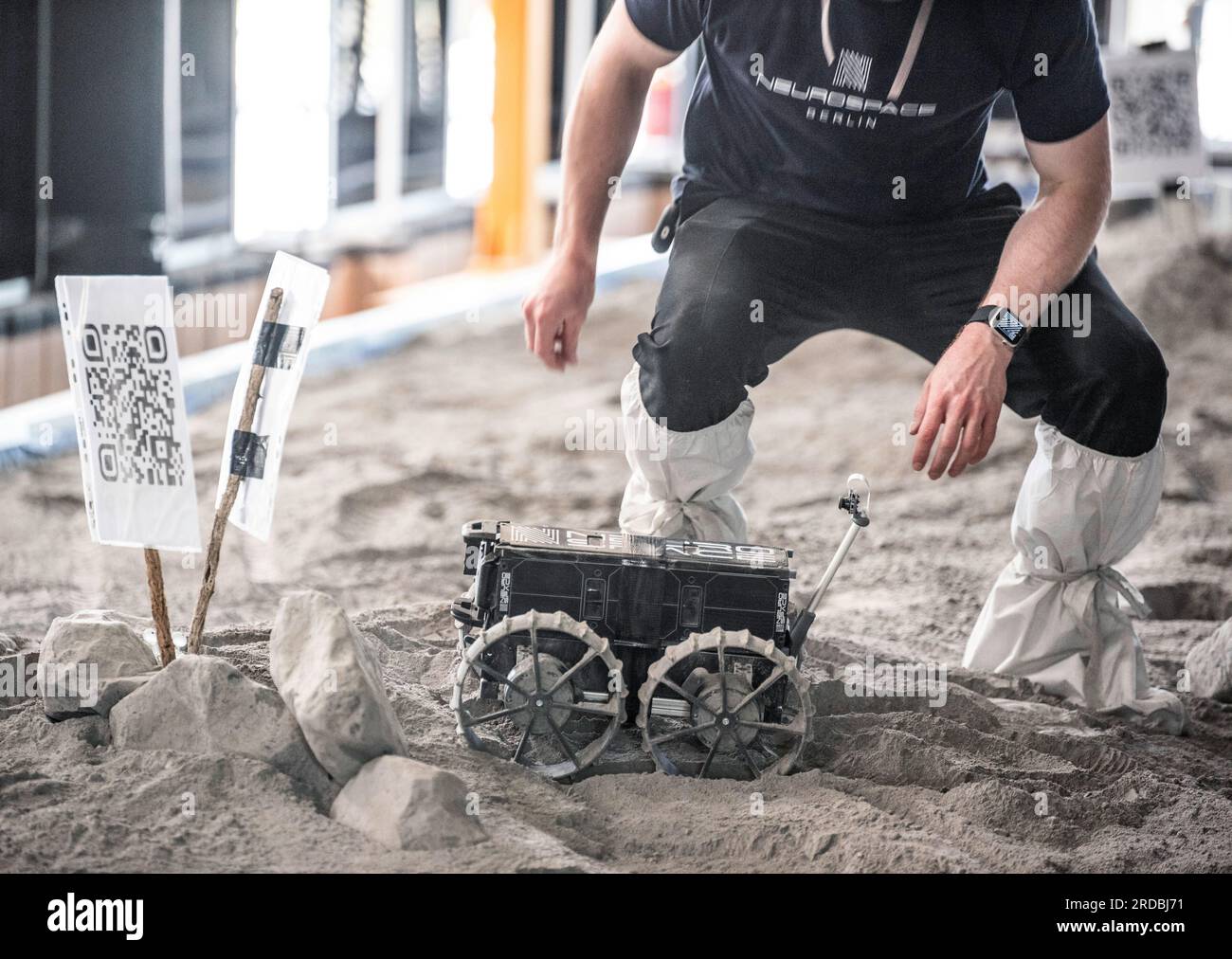 20 luglio 2023, Meclemburgo-Pomerania Occidentale, Rostock-Laage: L'ingegnere di sviluppo Max Manthey della Neurospace GmbH installa un rover lunare per un giro su un campo di prova nel terminal dell'aeroporto di Rostock-Laage. Il letto lunare costruito artificialmente nel terminal dell'aeroporto è lungo circa 18 metri, largo cinque metri e pieno di "polvere lunare" sulla superficie. In occasione della giornata internazionale della Luna che celebra il primo atterraggio con equipaggio il 20 luglio 1969, i piccoli rover di prova stanno ancora arando attraverso un paesaggio lunare creato artificialmente all'aeroporto di Rostock-Laage. Foto: Frank Horman Foto Stock 20 luglio 2023, Meclemburgo-Pomerania Occidentale, Rostock-Laage: L'ingegnere di sviluppo Max Manthey della Neurospace GmbH installa un rover lunare per un giro su un campo di prova nel terminal dell'aeroporto di Rostock-Laage. Il letto lunare costruito artificialmente nel terminal dell'aeroporto è lungo circa 18 metri, largo cinque metri e pieno di "polvere lunare" sulla superficie. In occasione della giornata internazionale della Luna che celebra il primo atterraggio con equipaggio il 20 luglio 1969, i piccoli rover di prova stanno ancora arando attraverso un paesaggio lunare creato artificialmente all'aeroporto di Rostock-Laage. Foto: Frank Horman Foto Stock