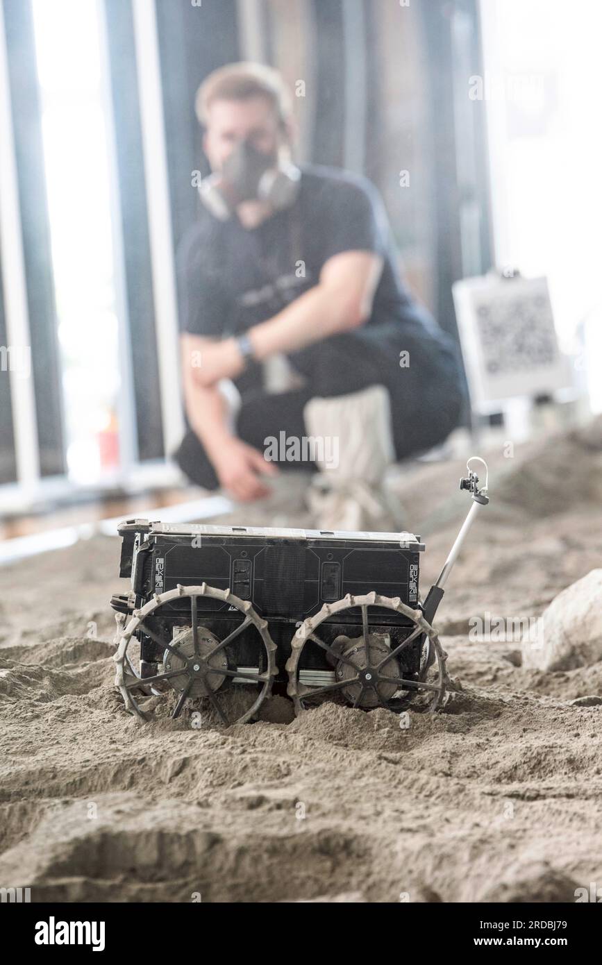 20 luglio 2023, Meclemburgo-Pomerania occidentale, Rostock-Laage: L'ingegnere di sviluppo Max Manthey della Neurospace GmbH osserva il viaggio di un rover lunare su un campo di prova nel terminal dell'aeroporto di Rostock-Laage. Il letto lunare costruito artificialmente nel terminal dell'aeroporto è lungo circa 18 metri, largo cinque metri e pieno di "polvere lunare" sulla superficie. In occasione della giornata internazionale della Luna che celebra il primo atterraggio con equipaggio il 20 luglio 1969, i piccoli rover di prova stanno ancora arando attraverso un paesaggio lunare creato artificialmente all'aeroporto di Rostock-Laage. Foto: Frank ho Foto Stock 20 luglio 2023, Meclemburgo-Pomerania occidentale, Rostock-Laage: L'ingegnere di sviluppo Max Manthey della Neurospace GmbH osserva il viaggio di un rover lunare su un campo di prova nel terminal dell'aeroporto di Rostock-Laage. Il letto lunare costruito artificialmente nel terminal dell'aeroporto è lungo circa 18 metri, largo cinque metri e pieno di "polvere lunare" sulla superficie. In occasione della giornata internazionale della Luna che celebra il primo atterraggio con equipaggio il 20 luglio 1969, i piccoli rover di prova stanno ancora arando attraverso un paesaggio lunare creato artificialmente all'aeroporto di Rostock-Laage. Foto: Frank ho Foto Stock