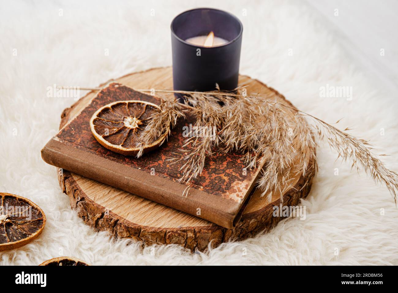 Libro di carta vintage su disco di legno di pino con canna secca e fetta di arancia secca. Aromi che bruciano le candele, oggetti sulla pelle di pecora. Accogliente set invernale autunnale. Foto Stock