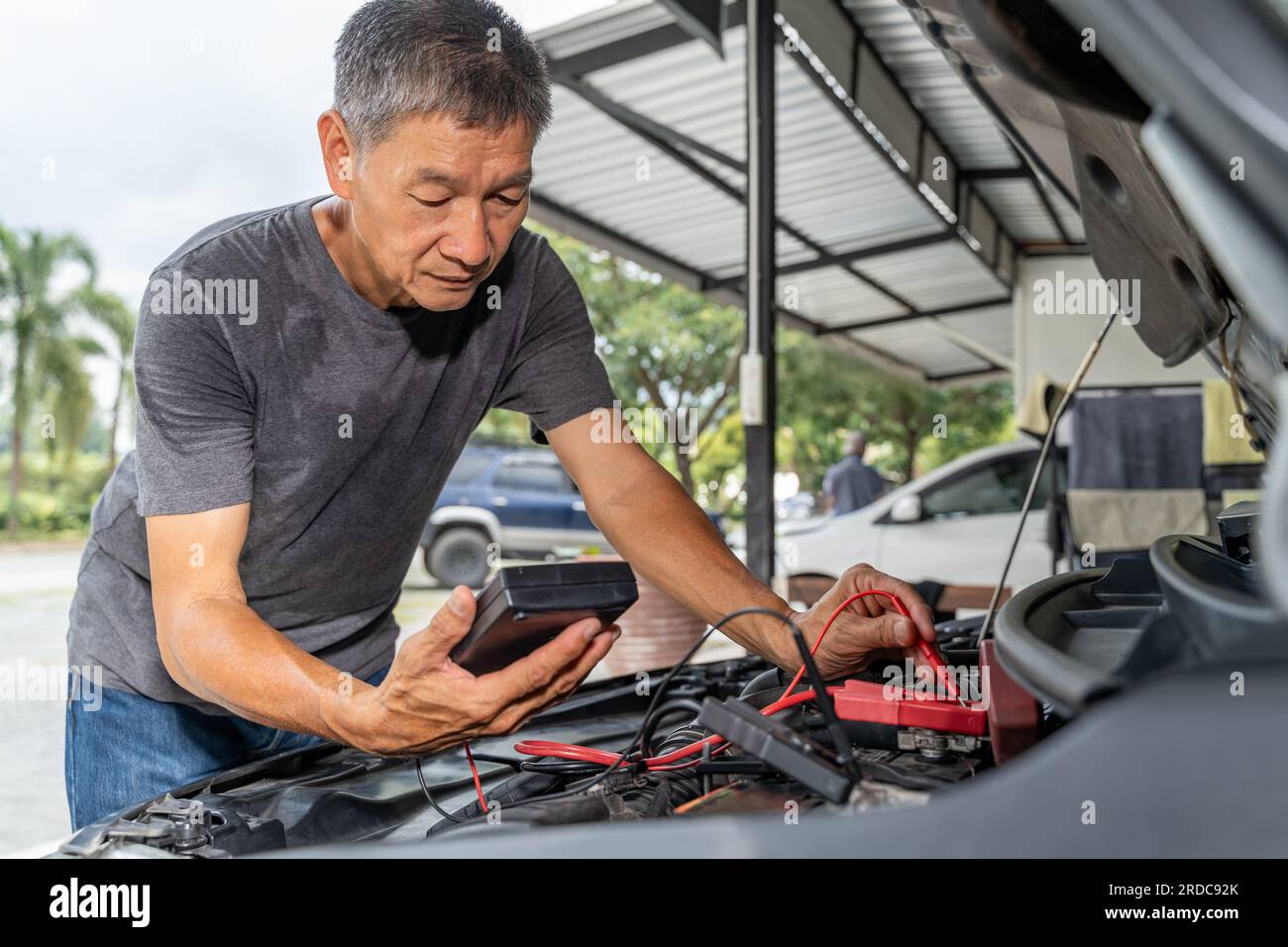 Un meccanico asiatico di mezza età che utilizza un tester per batterie per controllare lo stato della batteria della vettura Foto Stock