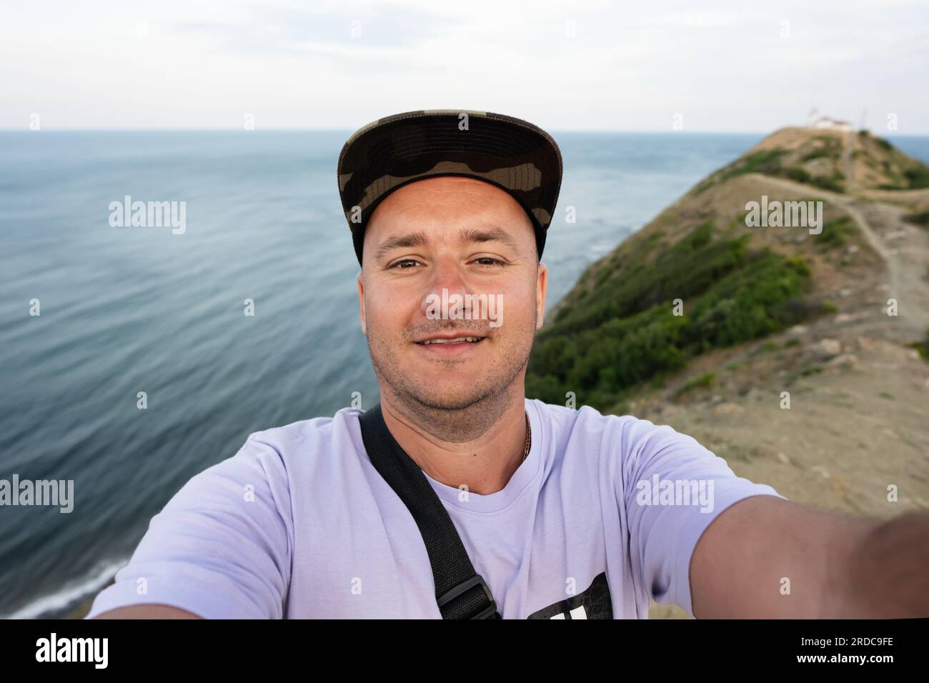 Ritratto di un uomo sorridente in cappellino che scatta un selfie sullo sfondo del mare. Capo Emine, costa del Mar Nero, Bulgaria. Foto Stock