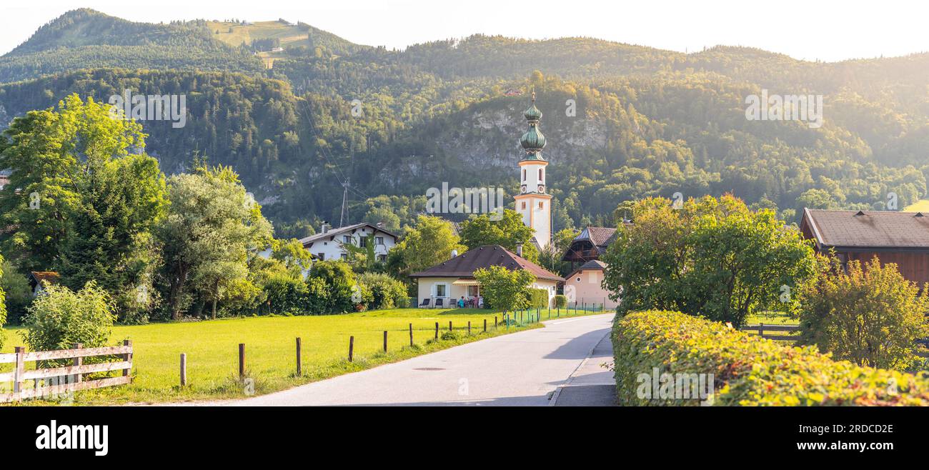 Paesaggio con strada e torre della chiesa nel villaggio di Sankt Gilgen, montagne di Zwolferhorn sullo sfondo, Alpi, Austria Foto Stock