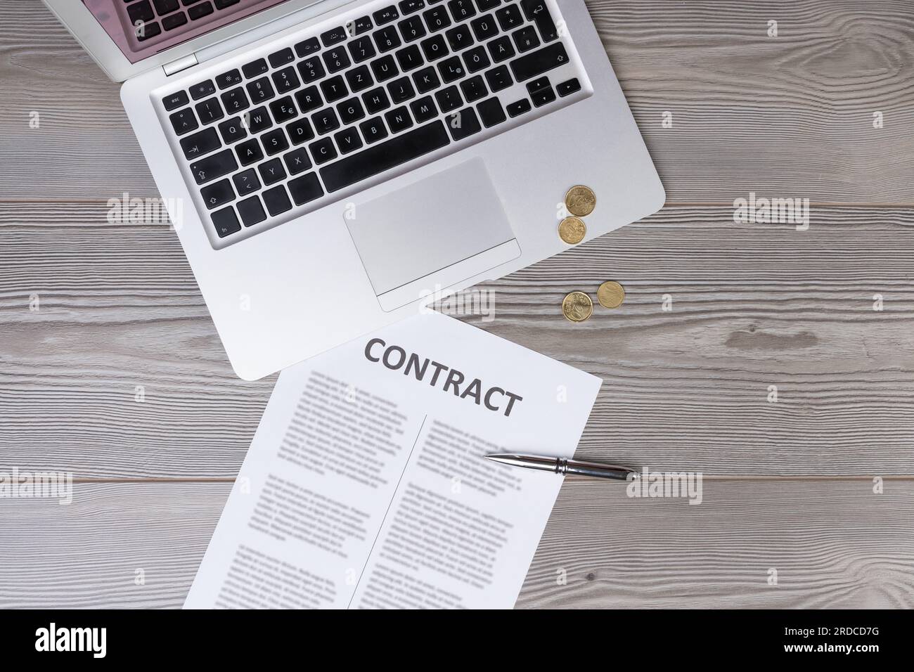 Vista dall'alto di una scrivania con un contratto, una penna, un laptop e monete d'oro, che illustra il concetto di commercio mediato dalla tecnologia, dalle aziende ai privati Foto Stock